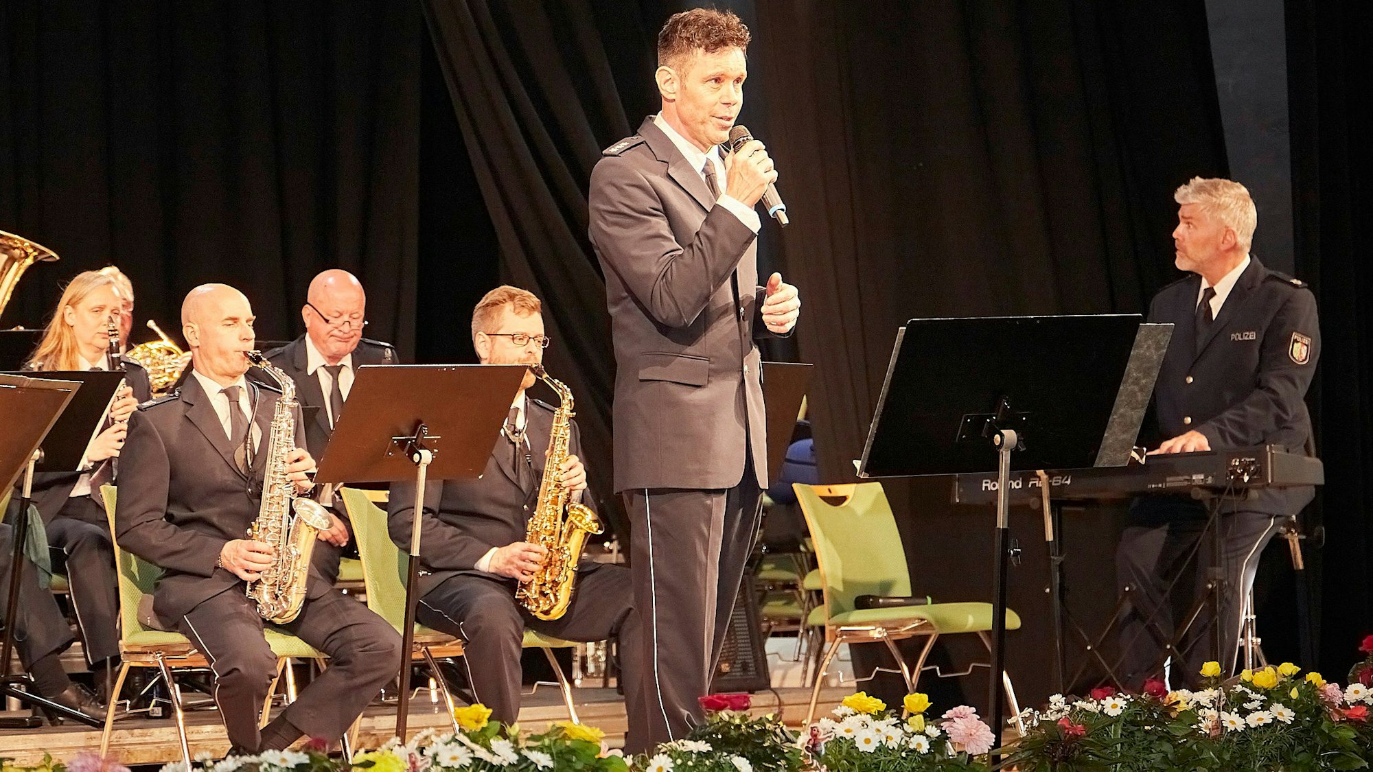 Musiker in Polizeiuniform geben im Gemünder Kursaal ein Konzert. Oliver Schmitt hält ein Mikrofon in der Hand und singt.