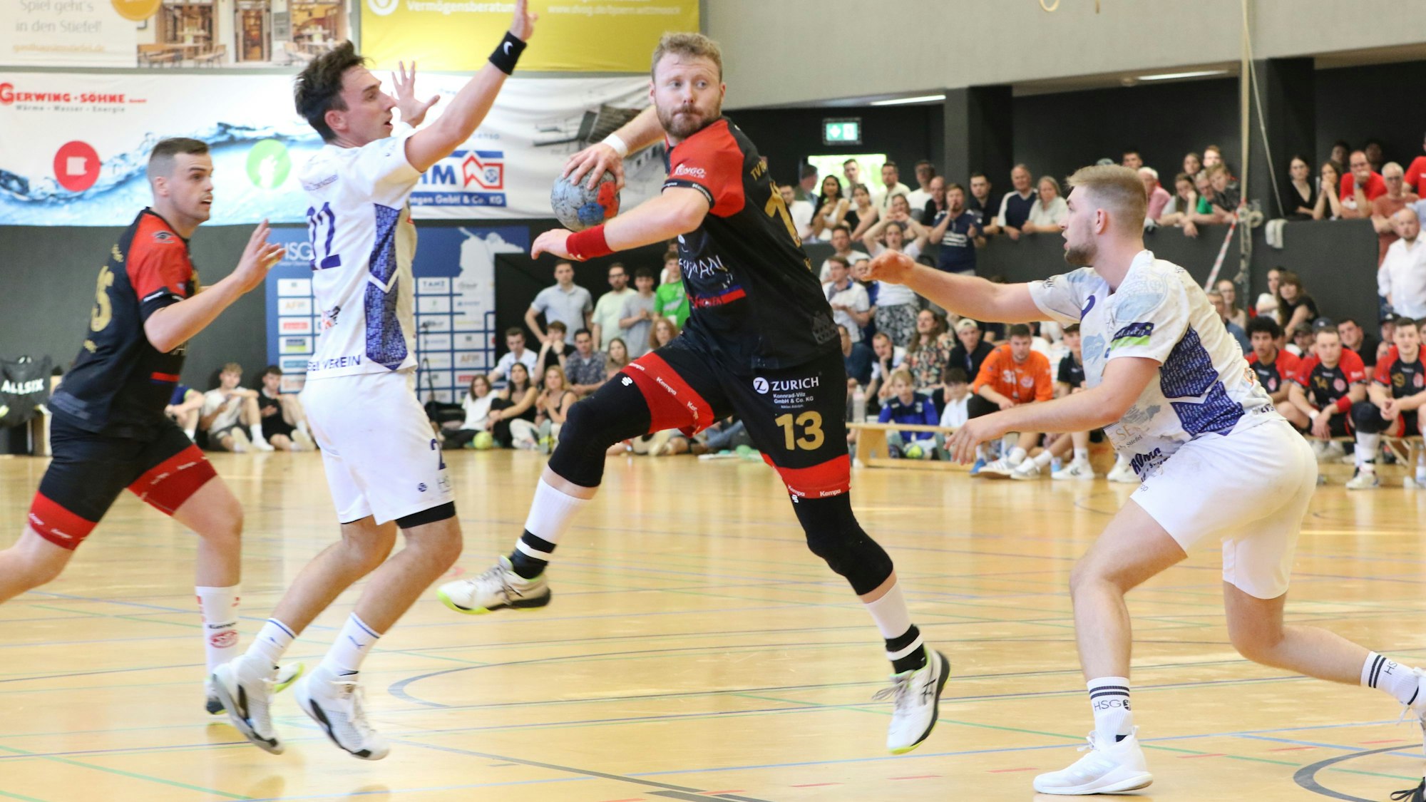 René Lönenbach setzt zum Wurf an, bedrängt von zwei Spielern. Im Hintergrund sieht man viele Zuschauer.