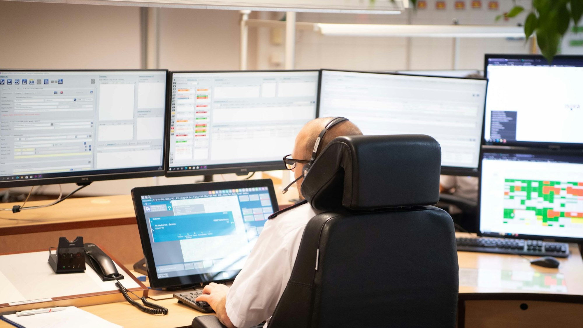 Das Bild zeigt einen Disponenten in der Leitstelle, der vor zahlreichen Monitoren sitzt.
