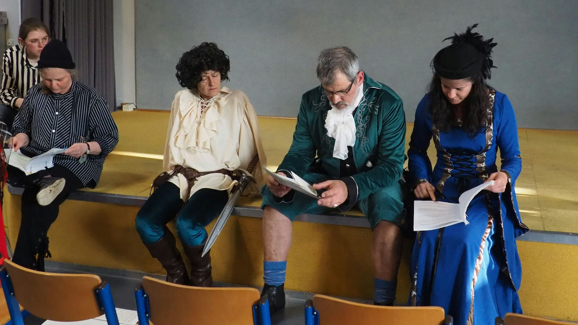 Die Schauspieler sitzen auf dem Rand der Bühne und studieren ihre Texthefte.