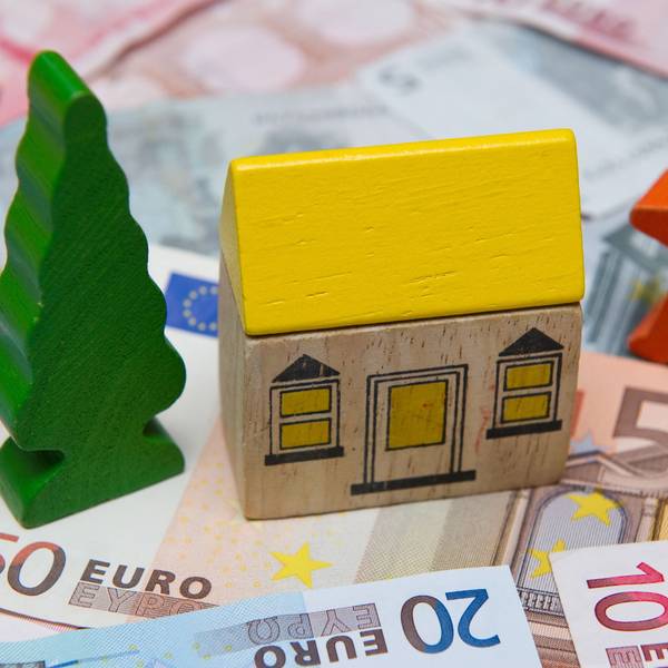 Ein kleines Spielzeughaus steht auf Euro-Geldscheinen.