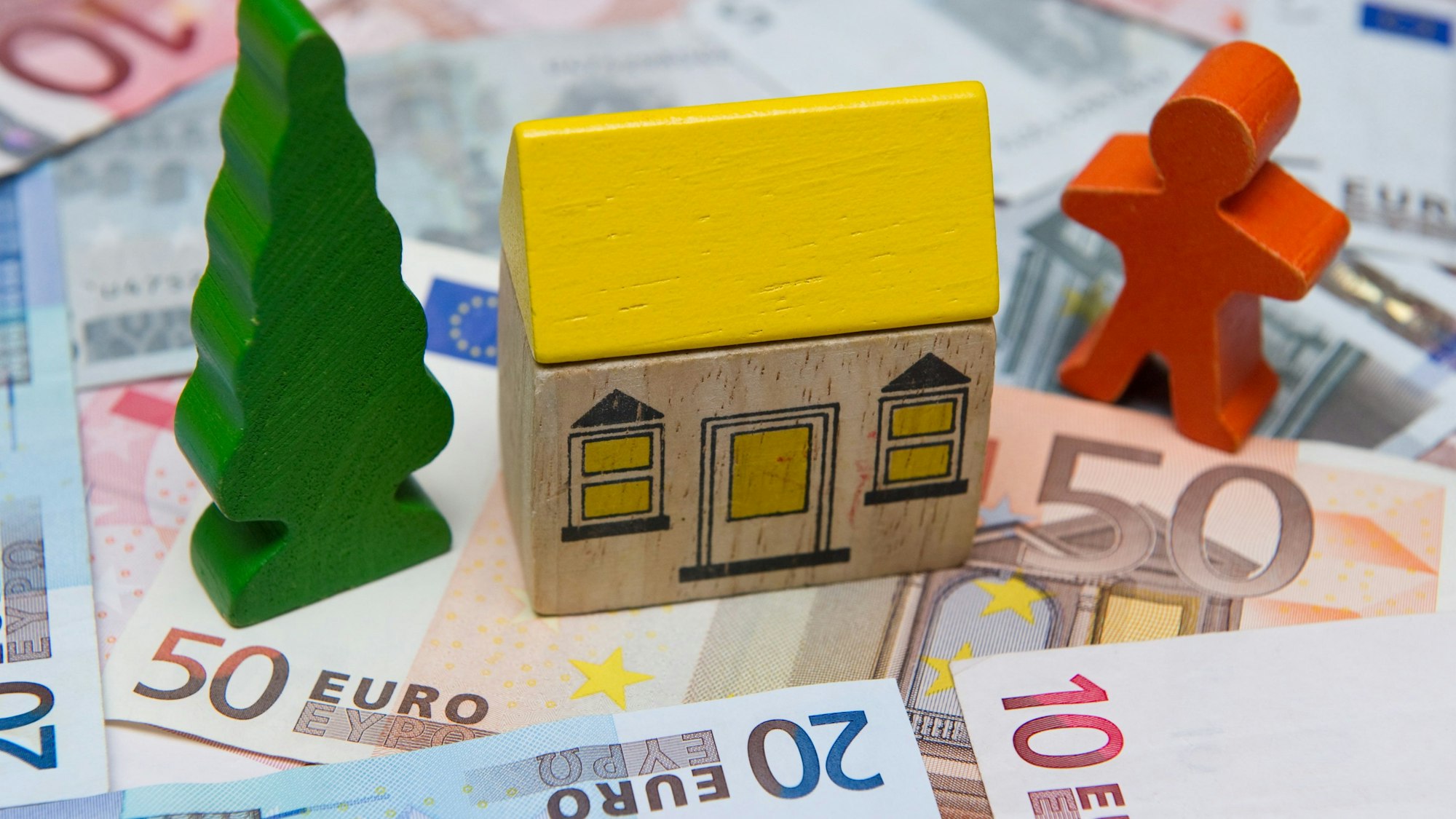 Ein kleines Spielzeughaus steht auf Euro-Geldscheinen.