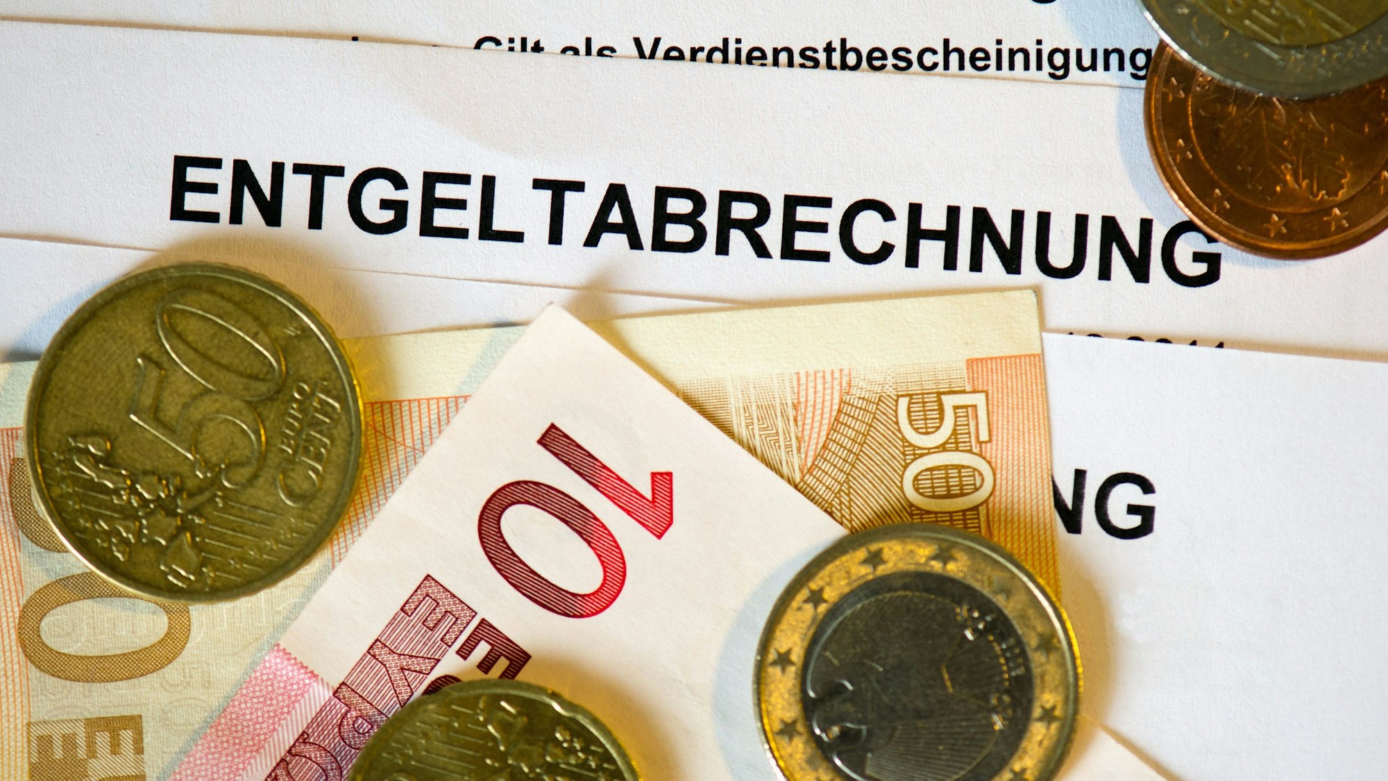 ARCHIV - 30.01.2013, Sachsen, Dresden: Auf Lohn- und Gehaltsabrechnungen (Entgeltabrechnungen) liegen Euromünzen und Eurogeldscheine.