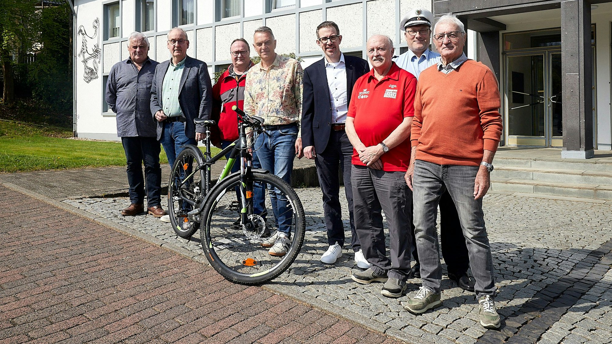Acht Männer stehen vor dem Rathaus in Hellenthal an einem Fahrrad.