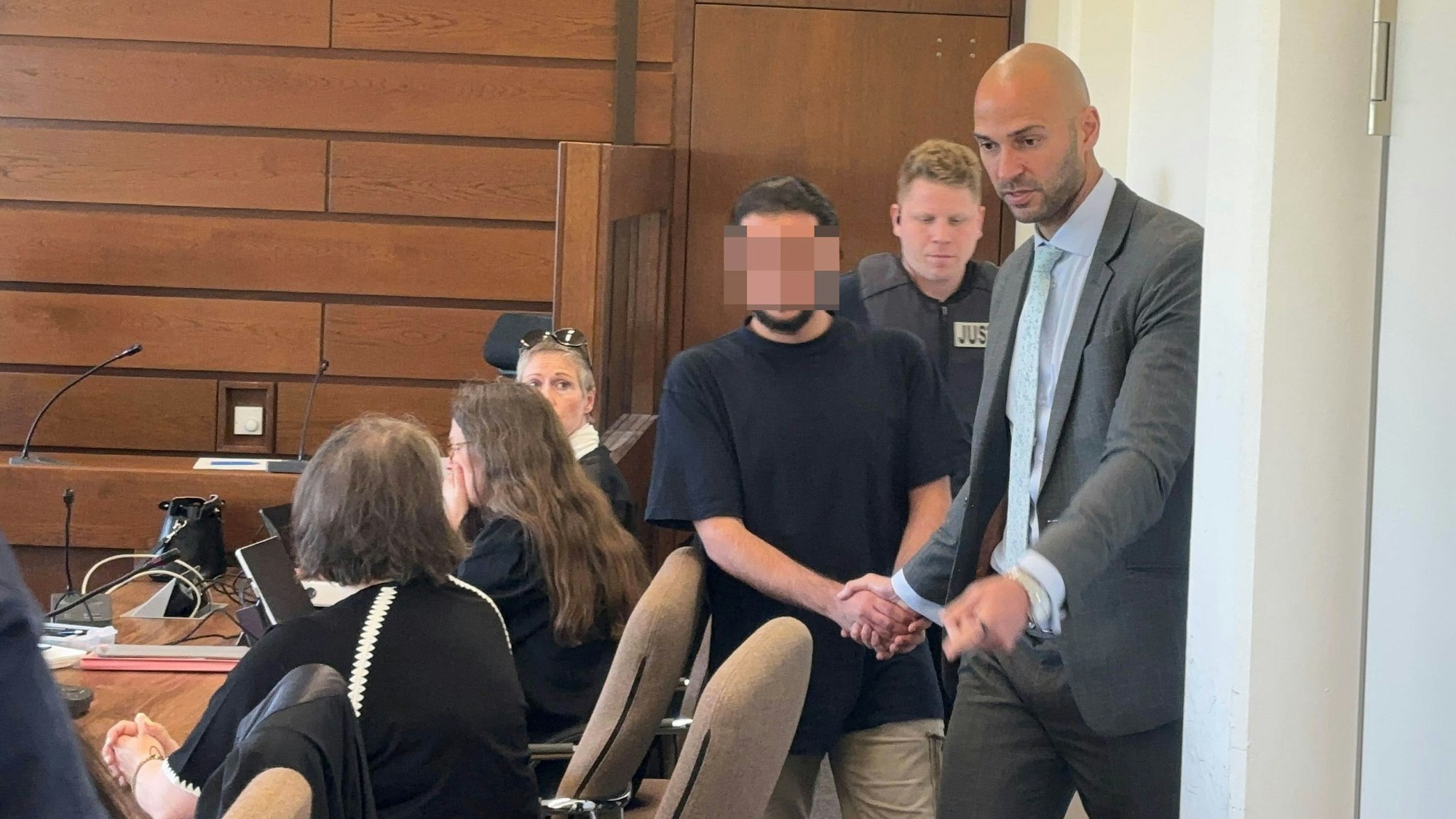 Das Bild zeigt, wie einer der Angeklagten in den Gerichtssaal gebracht wird.