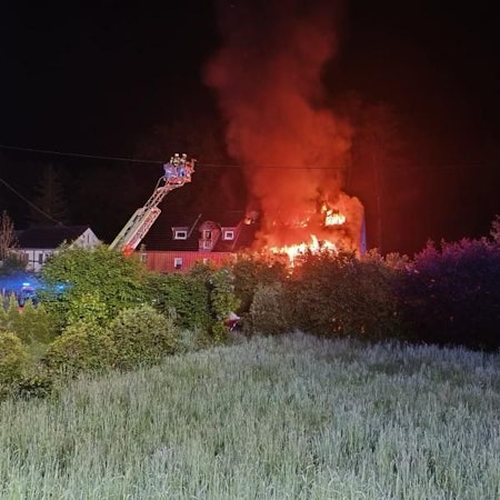 Ein Haus steht lichterloh in Flammen, die Feuerwehr löscht unter anderem mit Hilfe einer Drehleiter.
