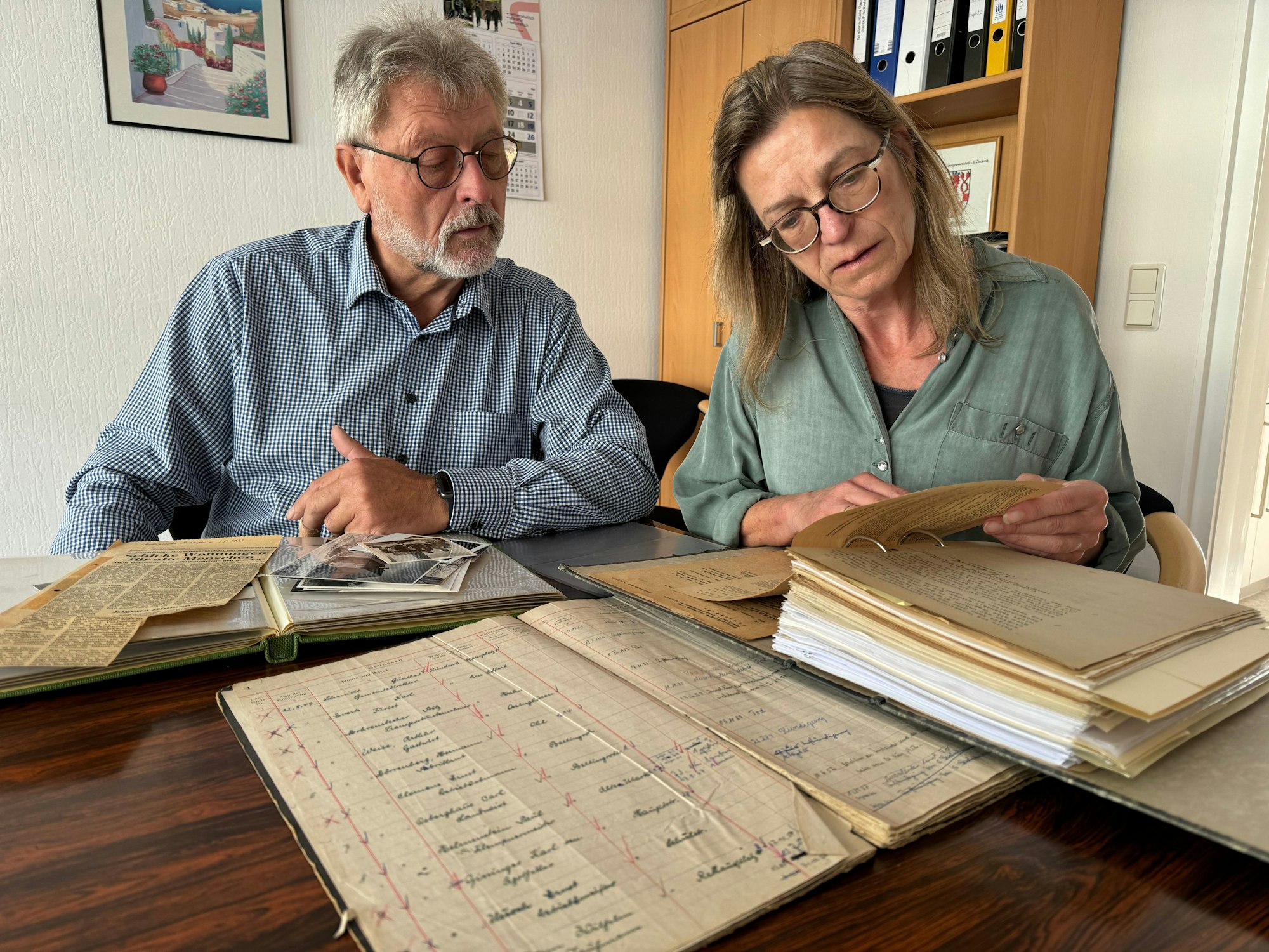 Zwei Menschen blättern in Aufzeichnungen aus den Anfangsjahren der Gemeinnützigen Baugenossenschaft Ründeroth, die Genossenschaft feiert 2024 ihr 75-Jähriges Bestehen.