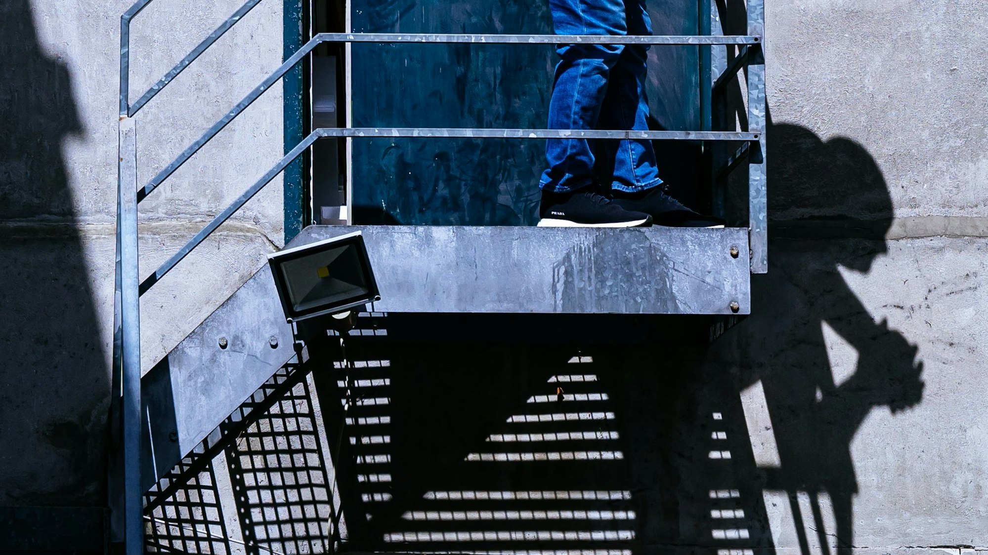 Schattenspiele: Ein Mann schaut von einer Eisentreppe auf die Straße.