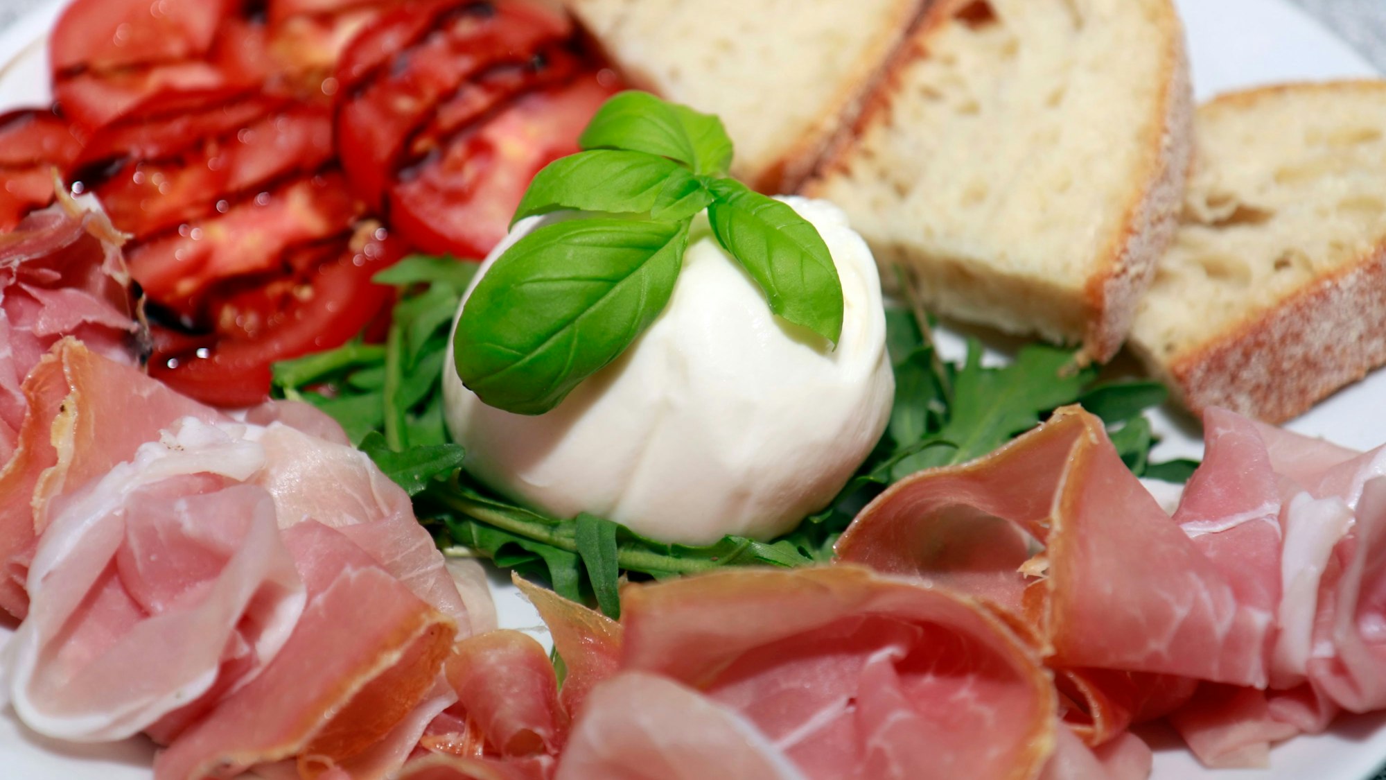 Schinken, Mozzarella, Tomaten und Brot liegen auf einem Teller.