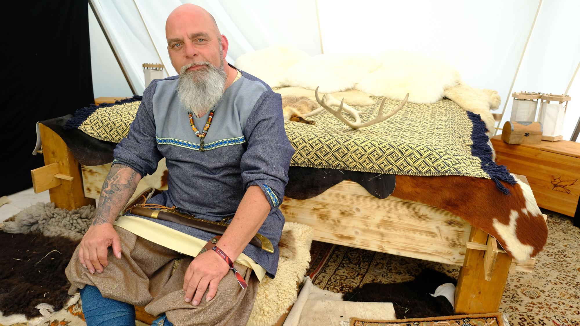 Berthold Nachtsheim sitzt als Wikinger auf einem Hocker, der vor einem Bett steht.