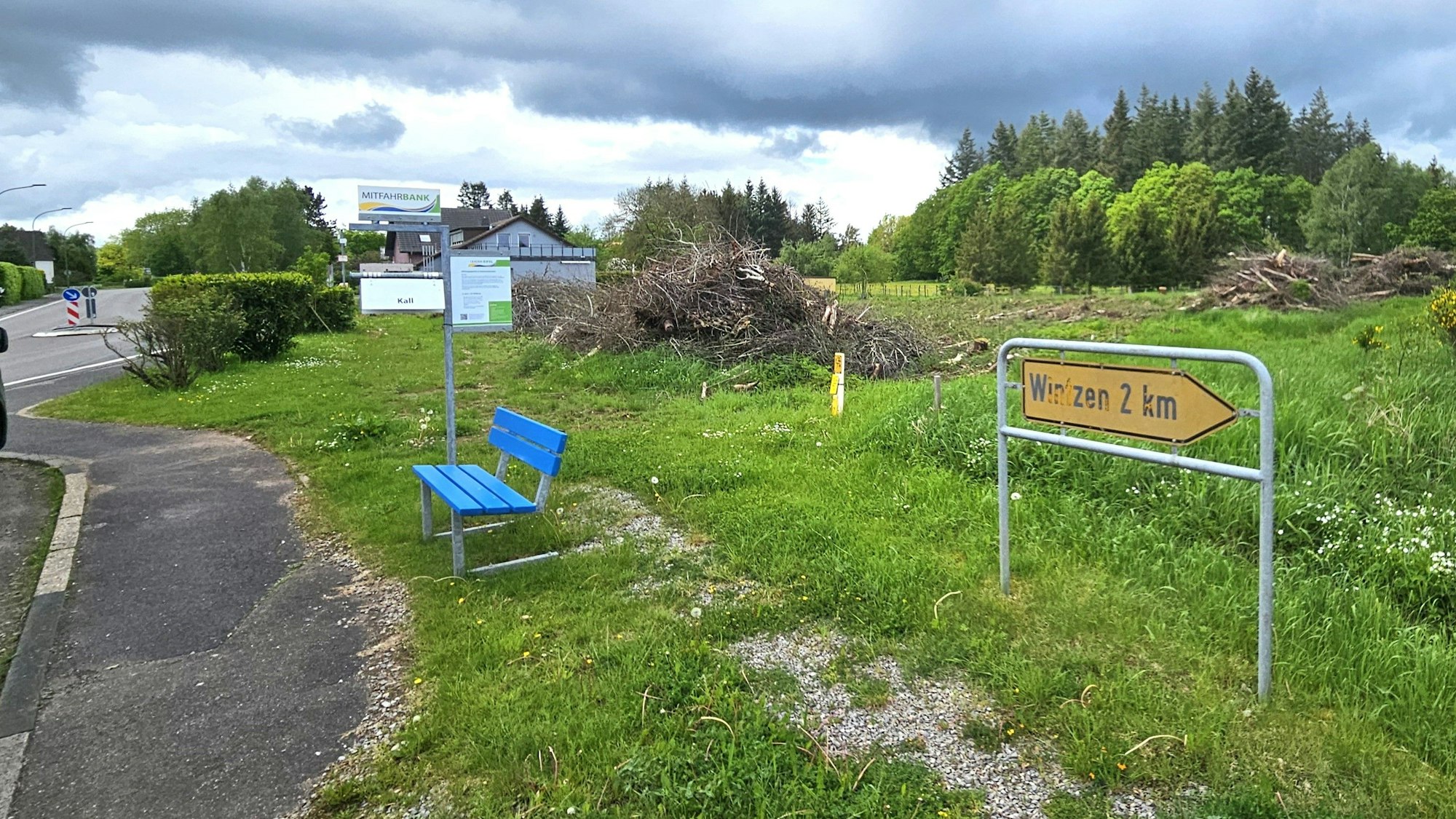 Blick auf ein Grundstück in Broich, das mit Sträuchern und Bäumen bewachsen ist. Ein Verkehrsschild weist den Weg ins zwei Kilometer entfernte Wintzen.