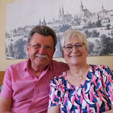 Die Eheleute sitzen auf einem Sofa und lächeln in die Kamera.