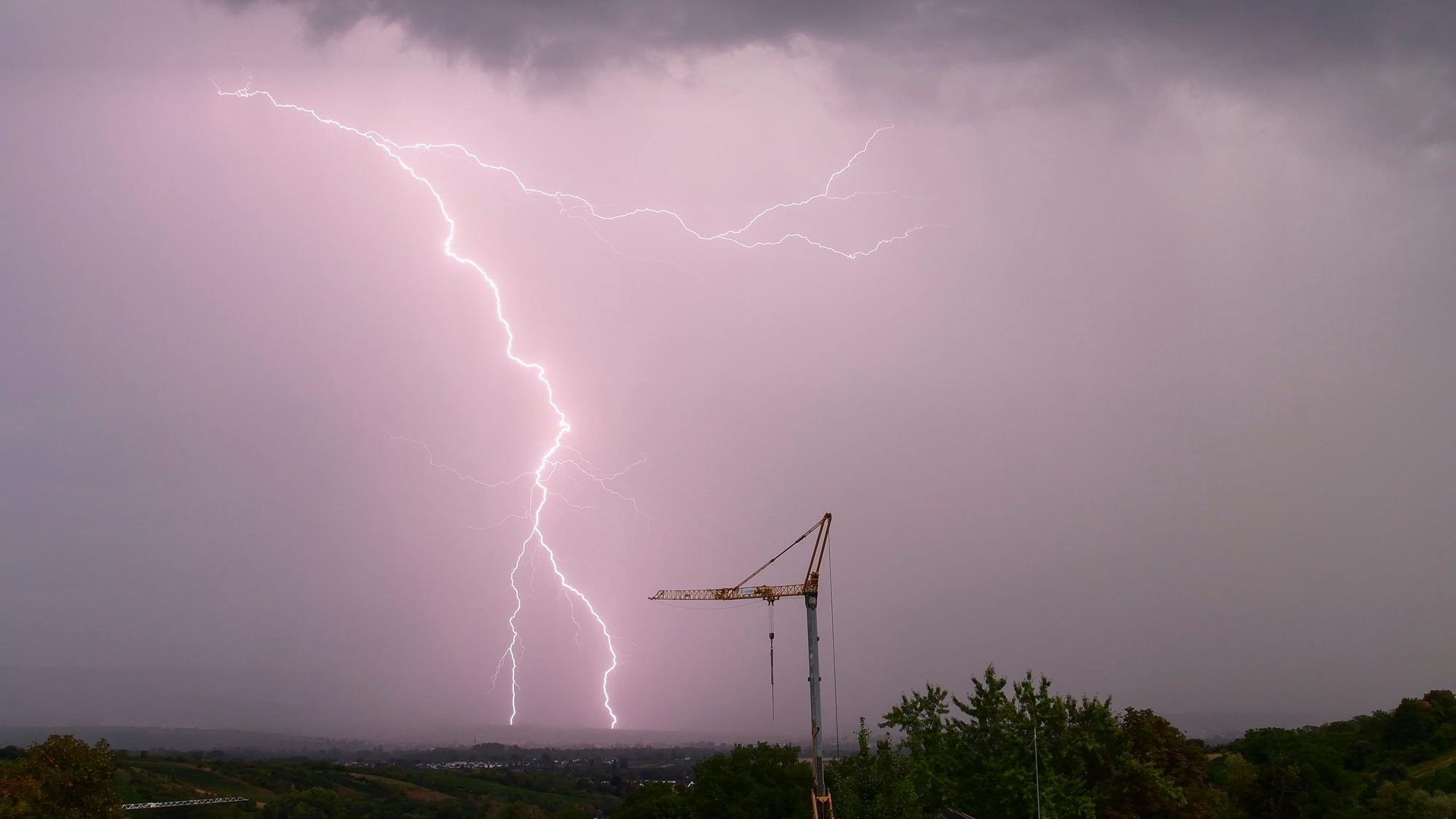 Ein gewaltiger Blitz schlägt am vom Unwetter lila gefärbten Himmel in der Nähe eines Baukrans ein. Schwere Unwetter werden in der Nacht zu Freitag in Köln und der Region erwartet. (Archivbild)