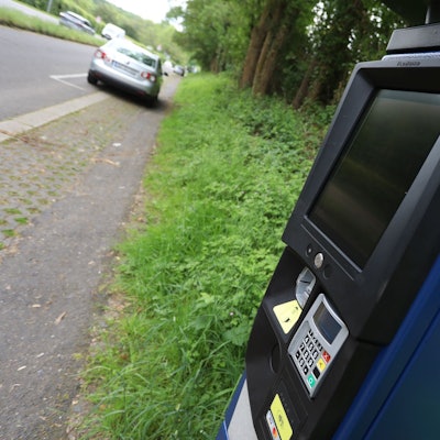 Ein Parkscheinautomat und ein parkendes Auto im Hintergrund.