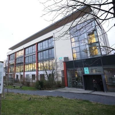 Ein Gebäude mit einer Bank davor, aus einigen Fenstern scheint Licht.