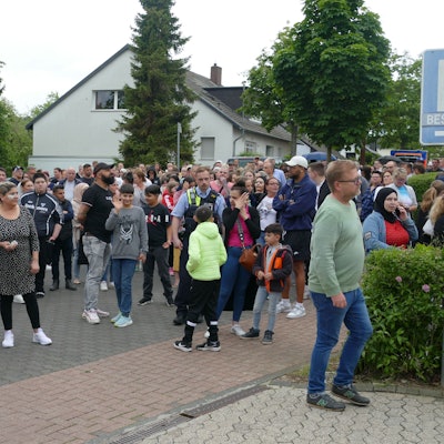 Eine größere Gruppe von Eltern und Angehörigen steht vor der Schule.