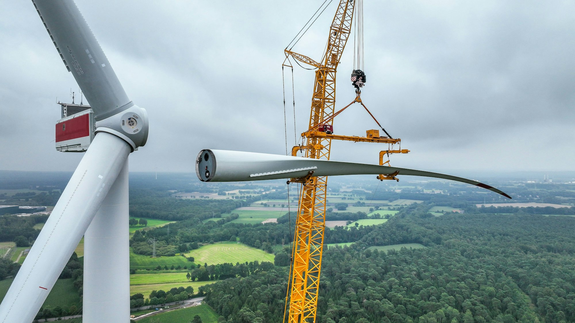 Bau einer Windenergieanlage. Ein mobiler Großkran hebt ein Rotorblatt zum Maschinenhaus auf den Turm.