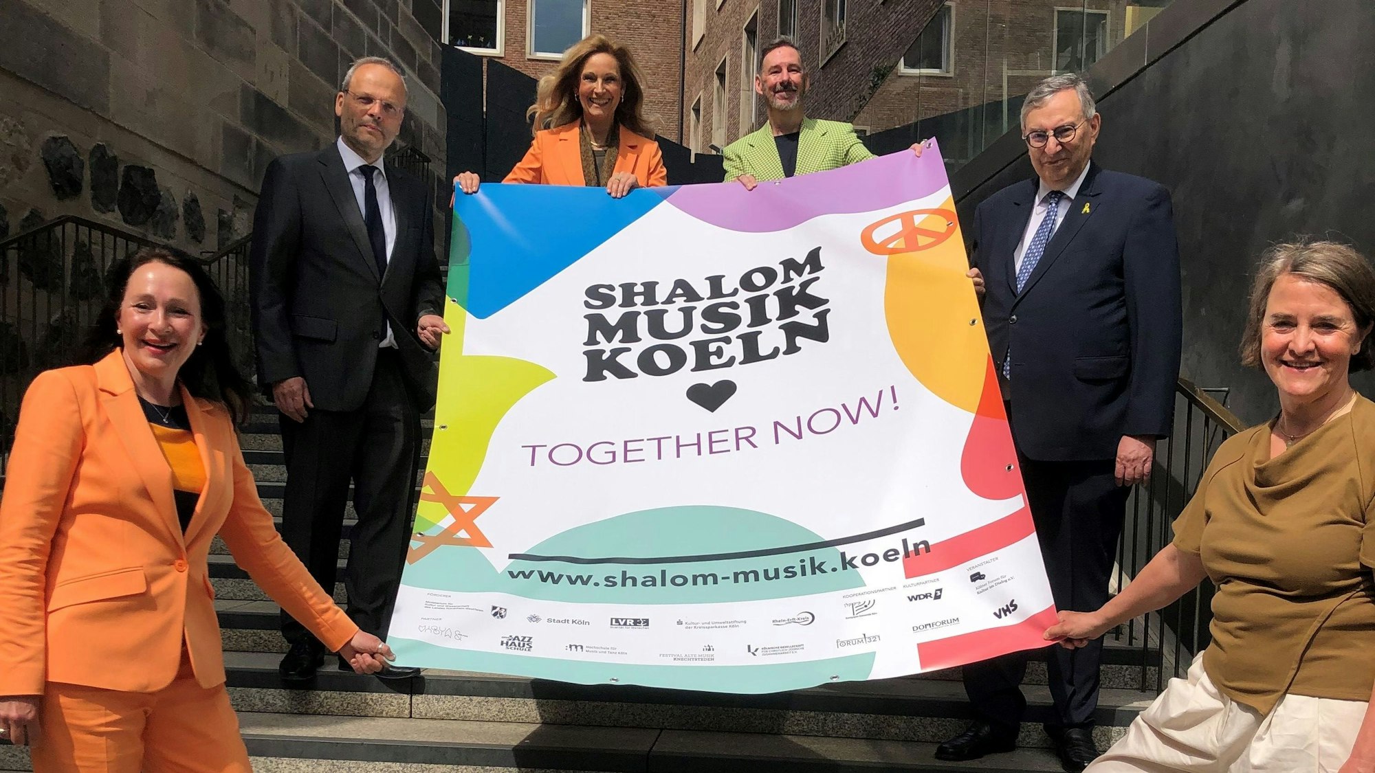 Die Organisatoren und Unterstützer stehen auf einer Treppe und halten ein Plakat fest.