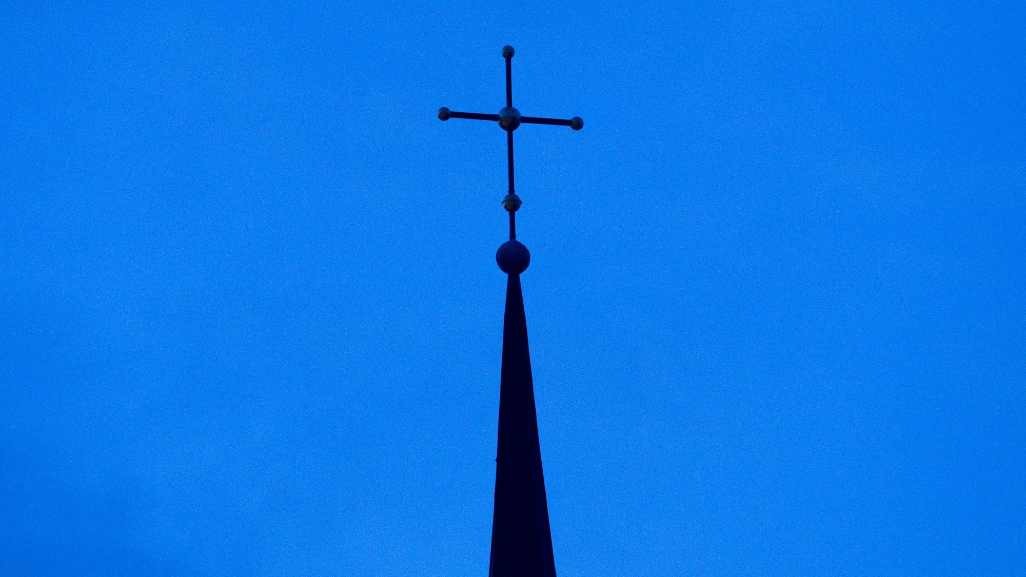 Das Kreuz einer evangelisch-lutherischen Kirche ist in der Abenddämmerung zu sehen.