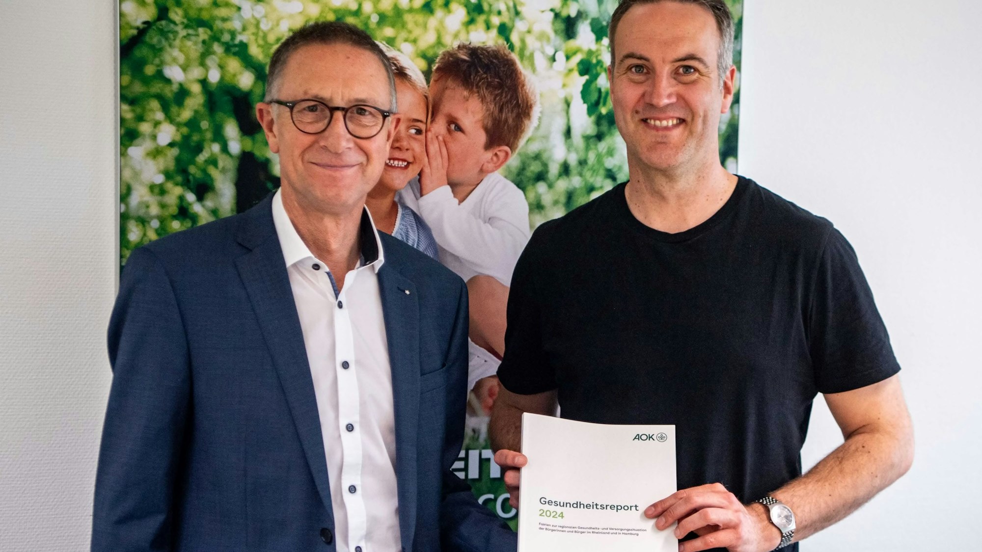 Das Bild zeigt den Regionaldirektor der AOK mit Dr. Volquart Stoy, der den Gesundheitsreport in den Händen hält.