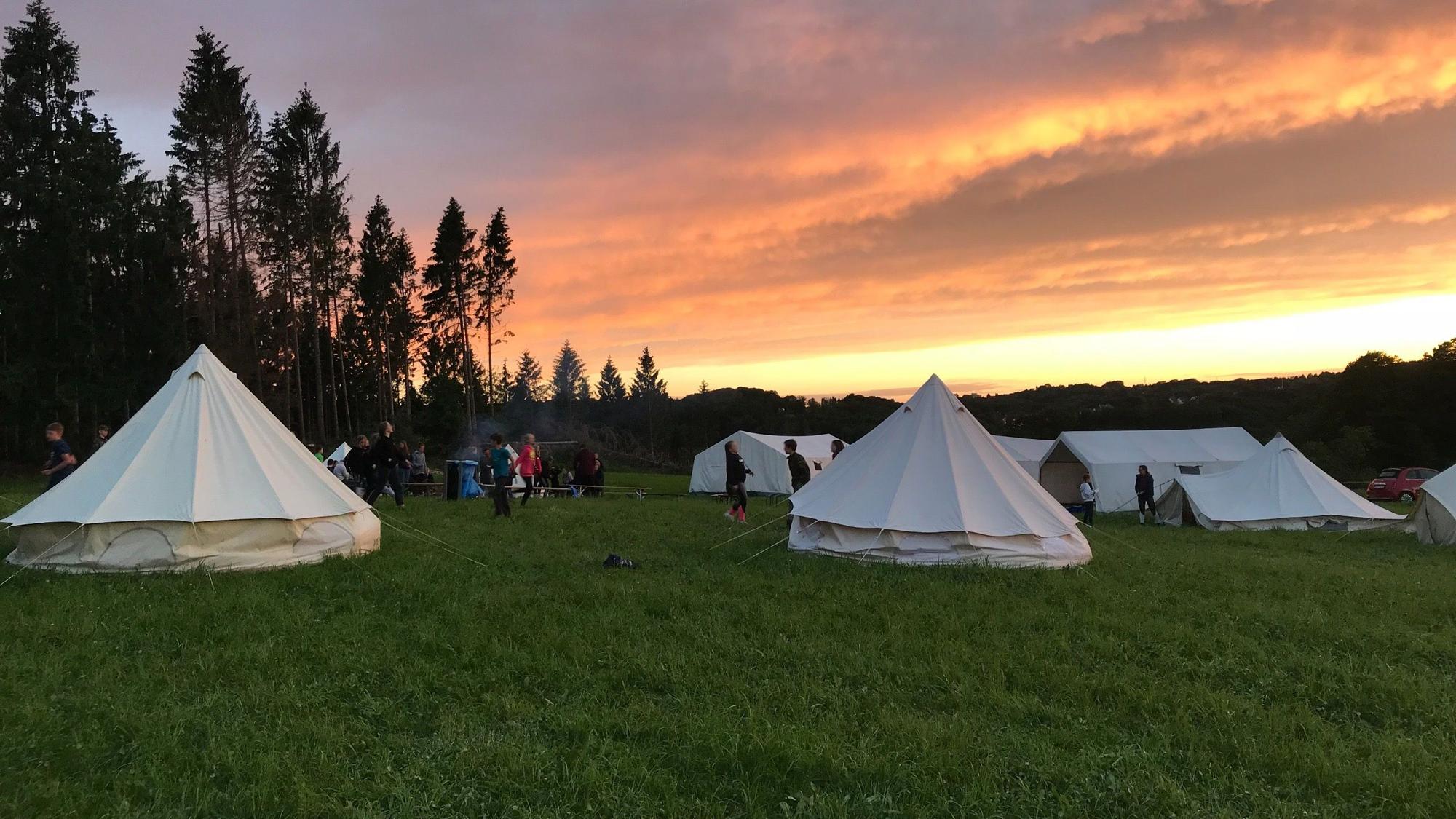 Zelte stehen auf einer Wiese im Abendrot.