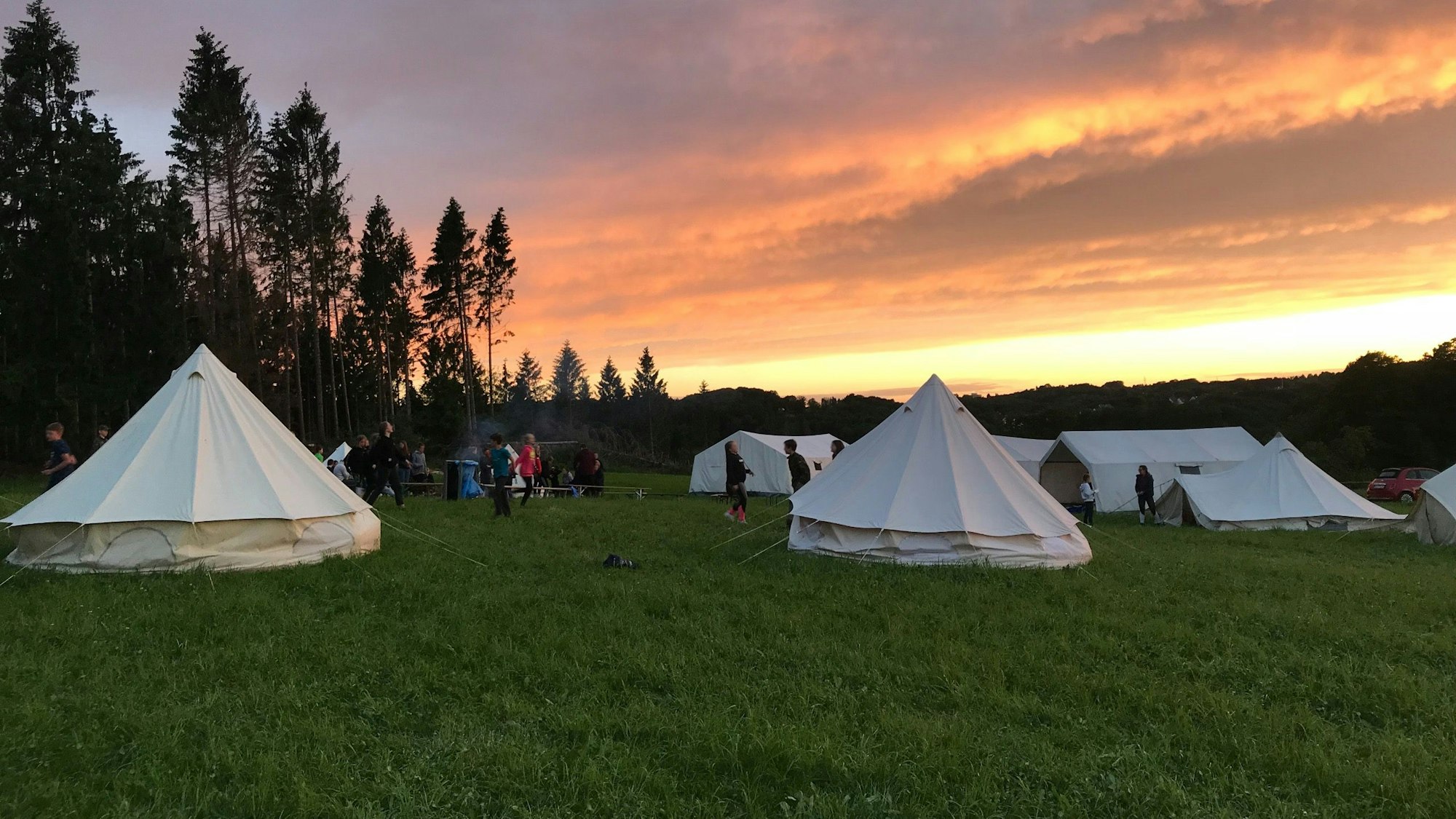 Zelte stehen auf einer Wiese im Abendrot.