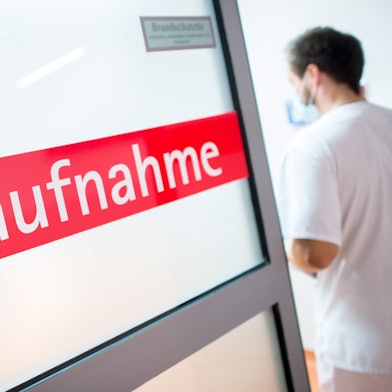 Ein Krankenpfleger tritt durch eine Glastür mit der Aufschrift "Notaufnahme".
