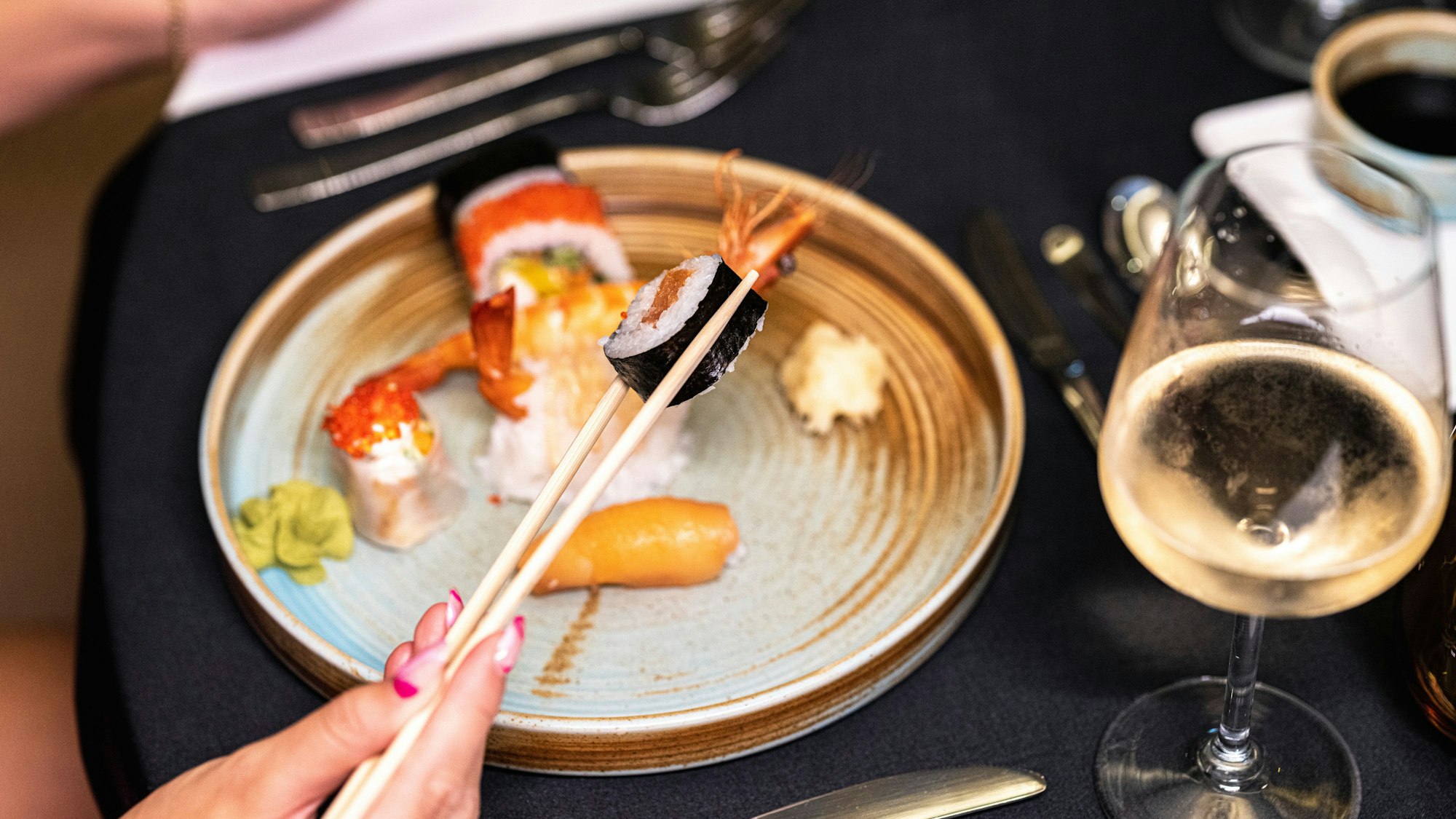 Eine Frau isst Sushi, daneben steht ein Glas Wein
