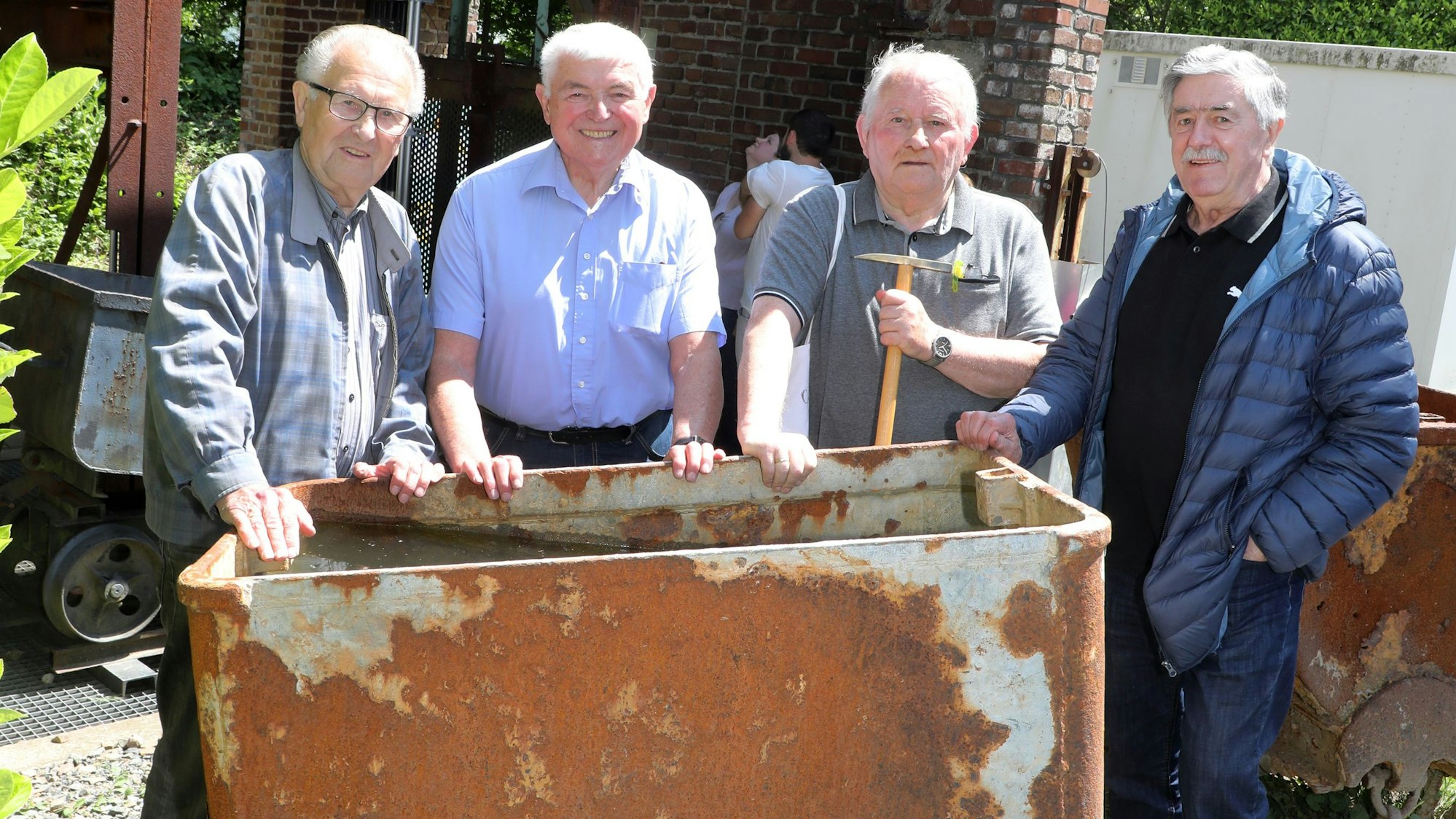 Siegfried Raimann mit ehemaligen Bergleuten an einem Grubenwagen unter dem Fördergerüst des Hauptschachts.