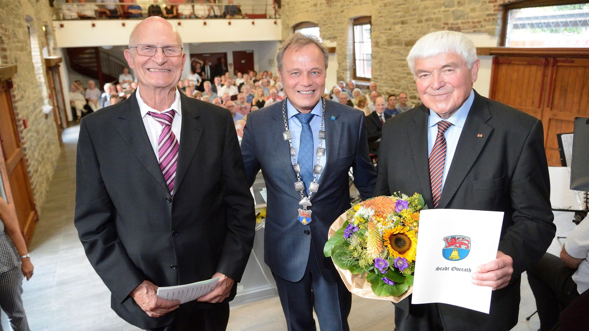 Die Overather Ehrenbürger Siegfried Raimann und Norbert Kuhl stehen mit Bürgermeister Jörg Weigt im Jahr 2018 auf der Bühne des Kulturbahnhofs Overath.