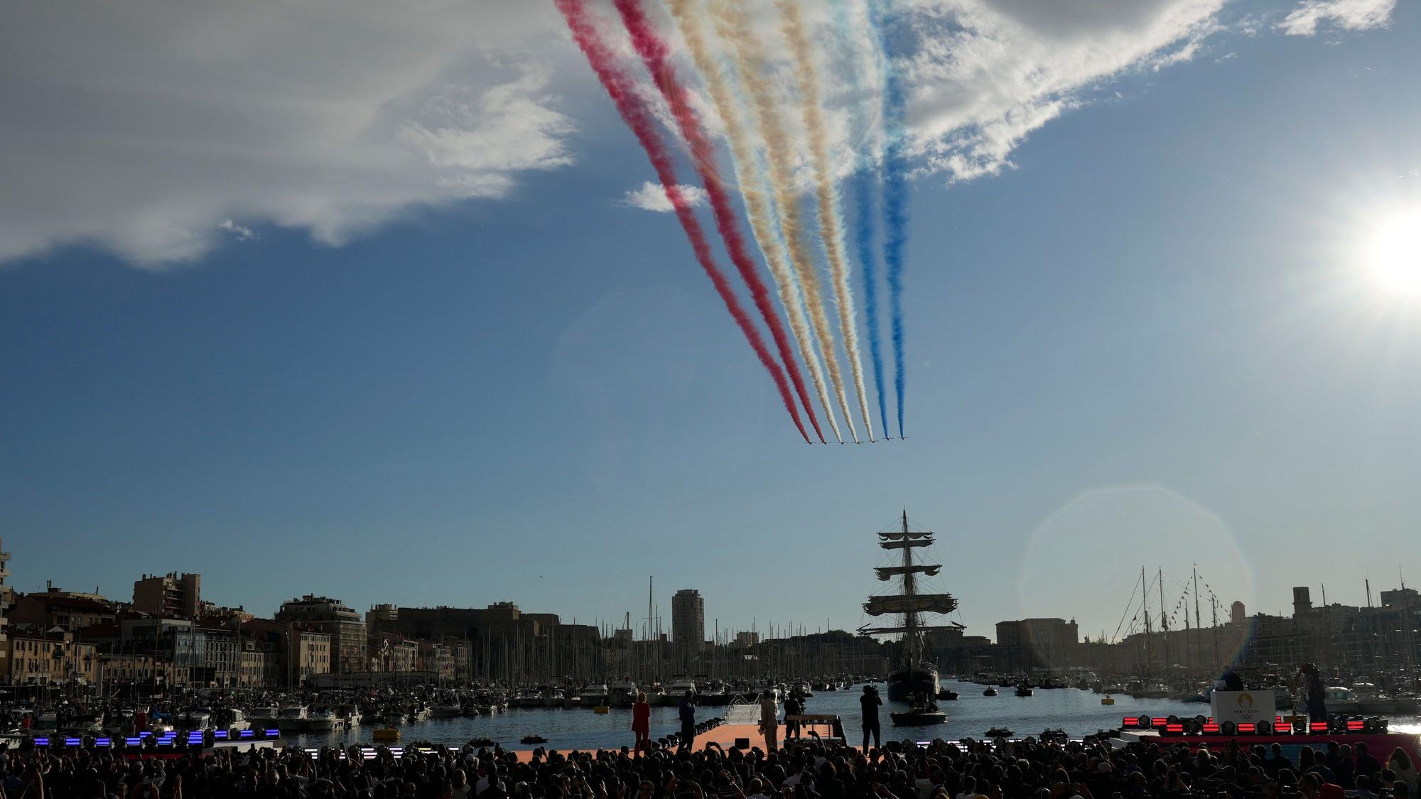 Marseille: Die Flugzeuge der „Patrouille de France“ hinterlassen Rauch in den Farben der französischen Fahne am Himmel, während die „Belem“, das dreimastige Segelschiff, das die olympische Flamme transportiert, in den Alten Hafen von Marseille einläuft.