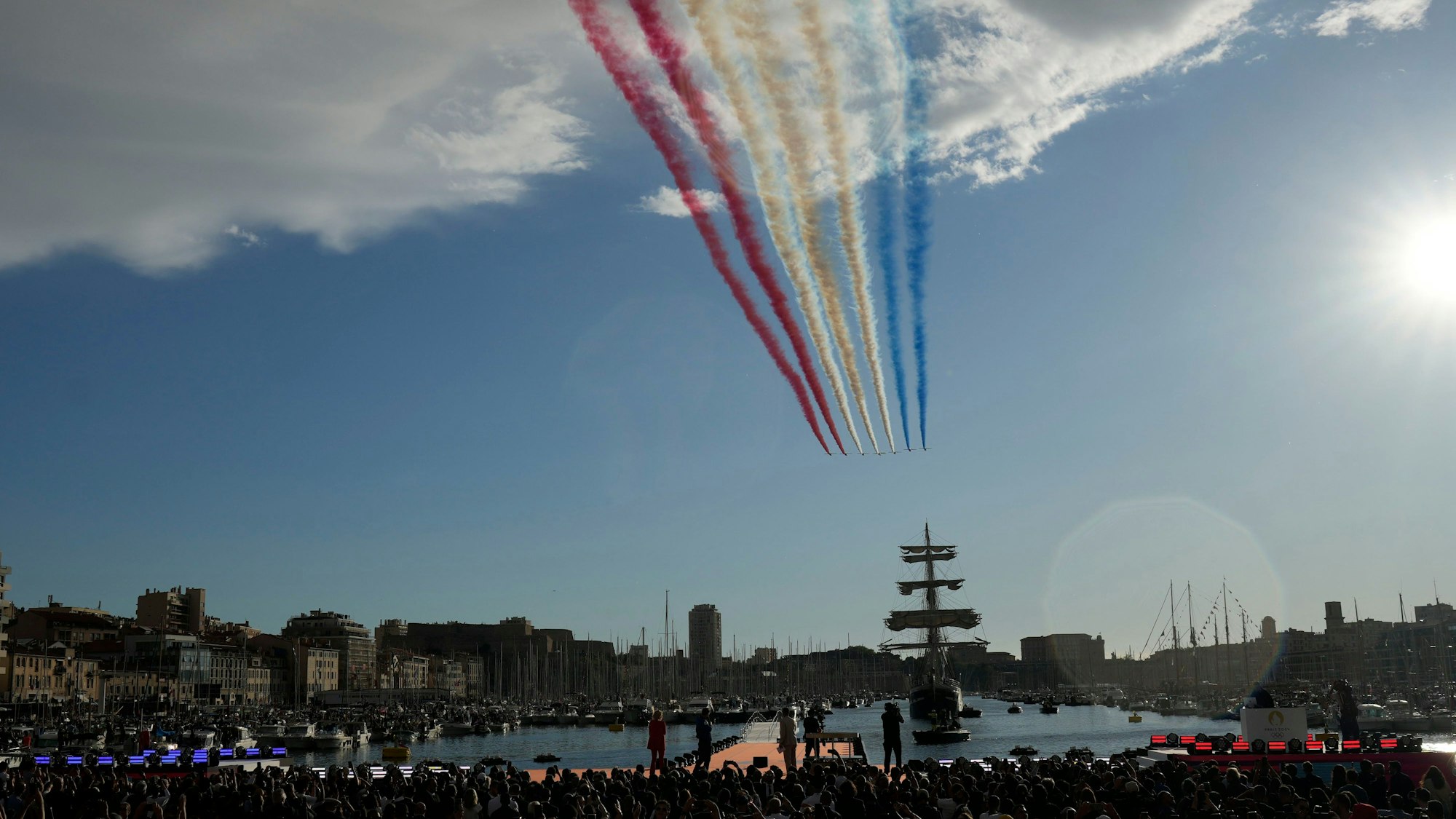 Marseille: Die Flugzeuge der „Patrouille de France“ hinterlassen Rauch in den Farben der französischen Fahne am Himmel, während die „Belem“, das dreimastige Segelschiff, das die olympische Flamme transportiert, in den Alten Hafen von Marseille einläuft.