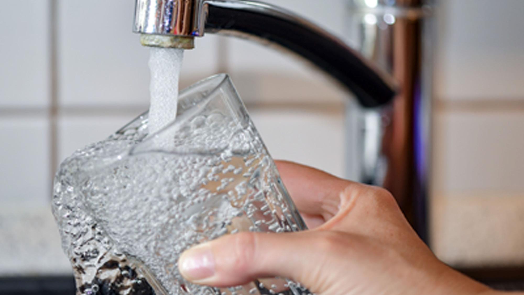 Eine Person hält ein Glas unter einen geöffneten Wasserhahn.