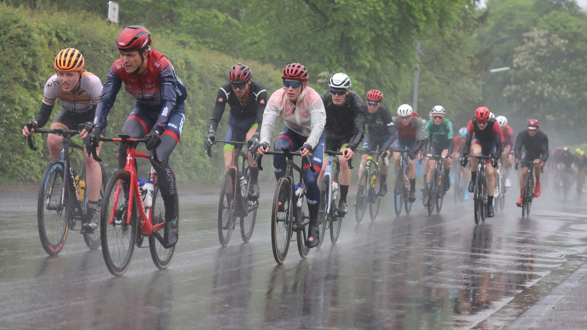 Radrennfahrer befahren im strömenden Regen eine Straße in Hellenthal-Rescheid.