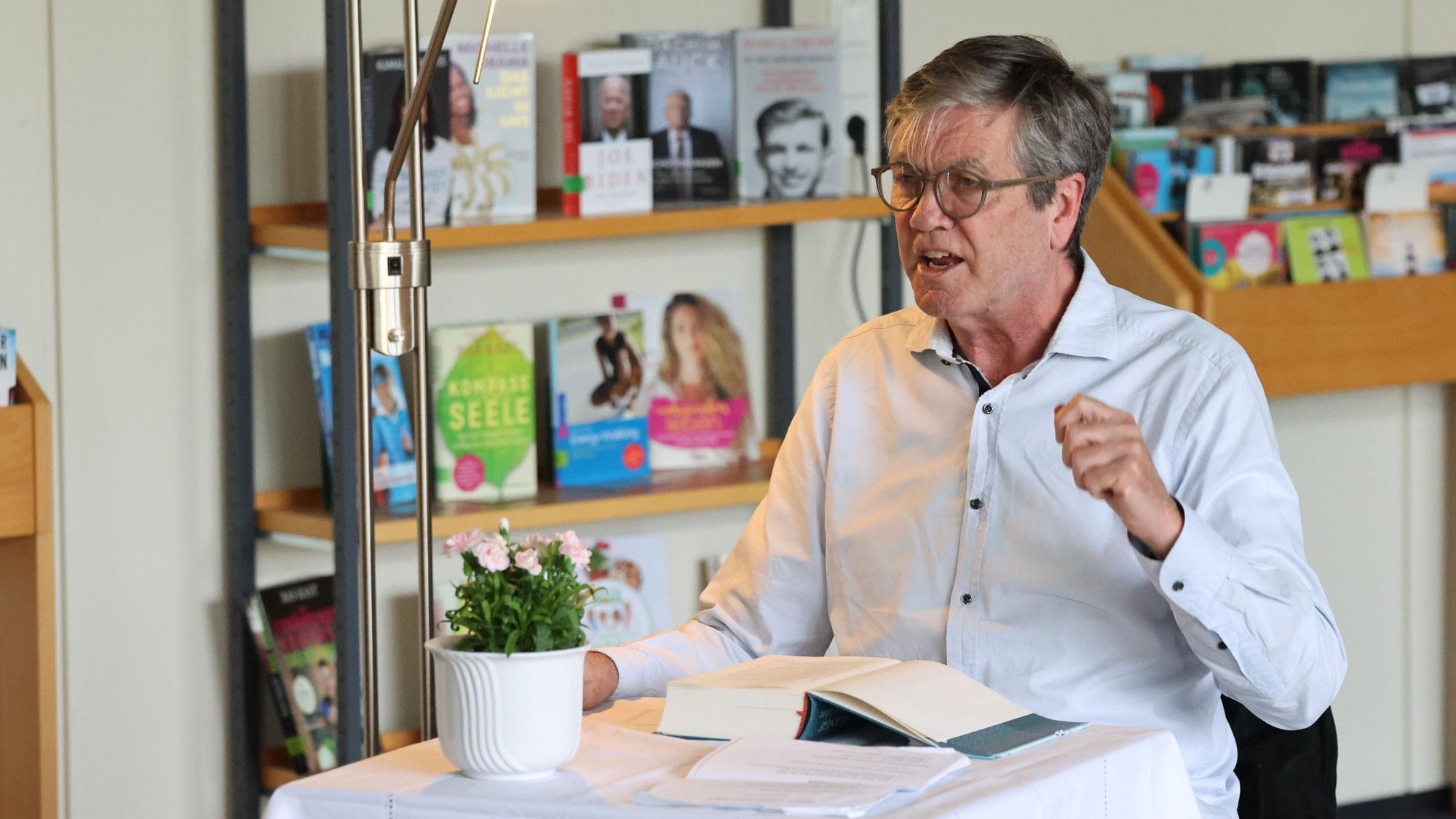 Peter Prange sitzt mit einem Buch an einem Tisch.