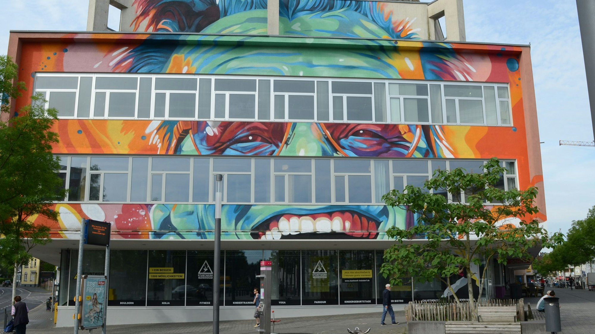 Ein Kaufhausgebäude aus den 70er Jahren. Es ist in grellen Farben bemalt; zu erkennen sind Augen, Zähne und Haare.