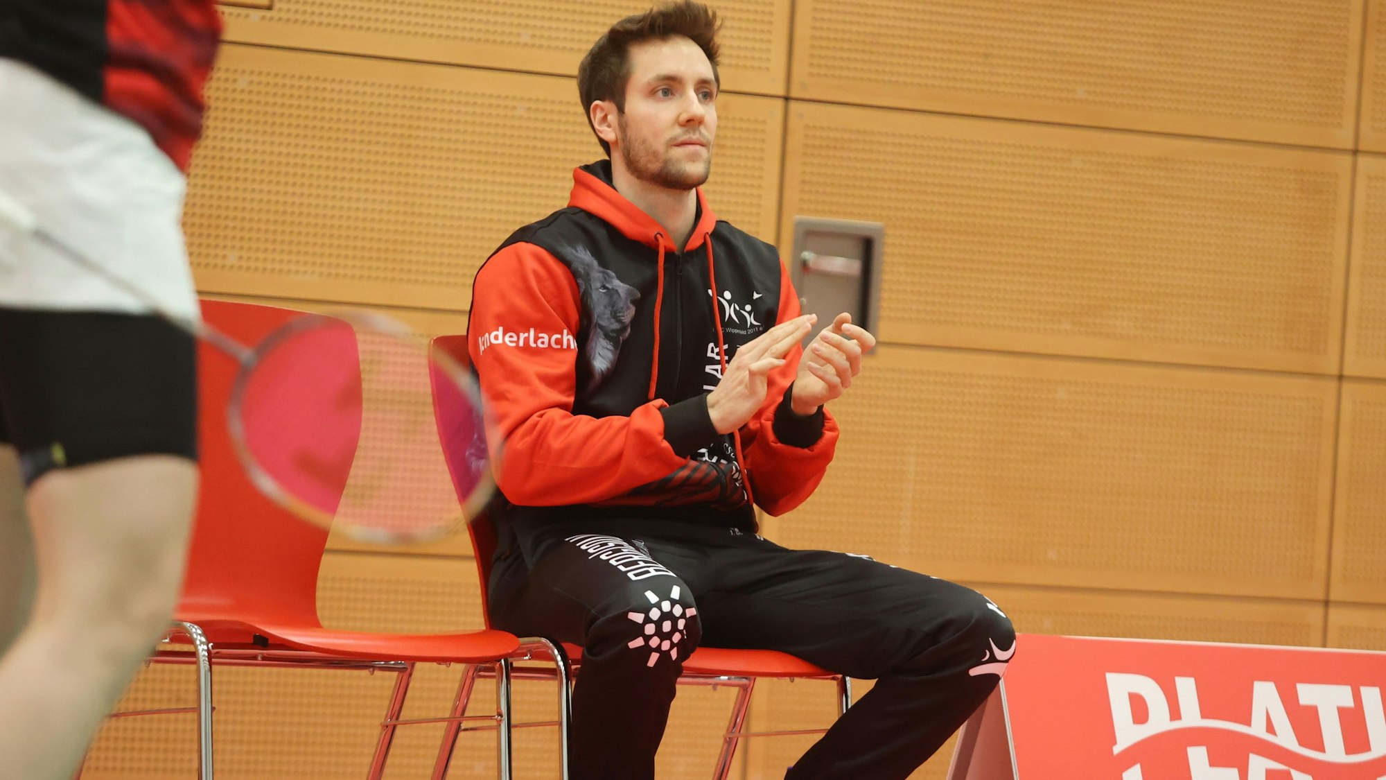 Blick auf einen Sportler, der auf einem Stuhl ein Badmintonspiel verfolgt.