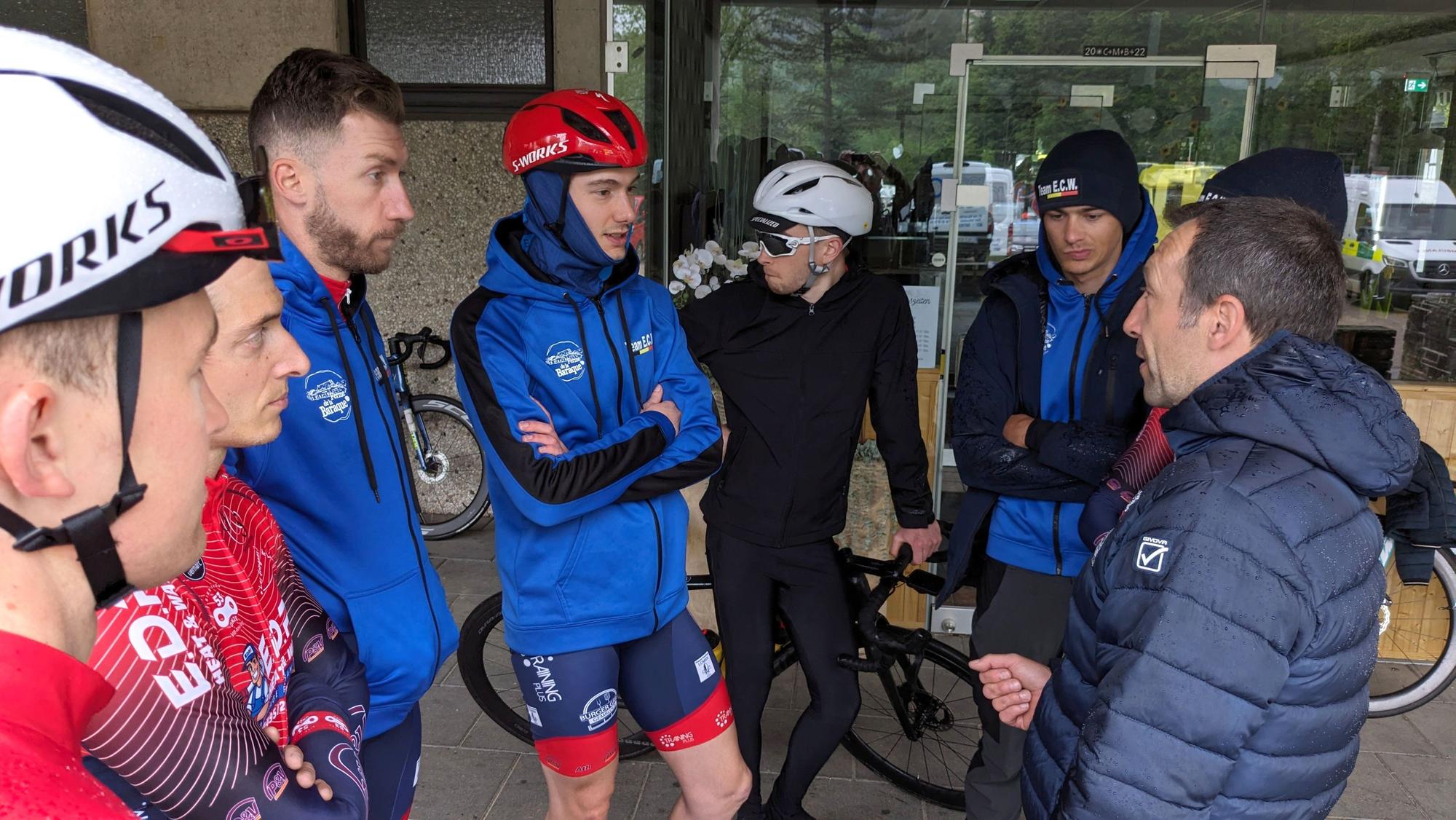 Radrennfahrer stehen vor dem Start in einer Gruppe bei ihrem Sportlichen Leiter.