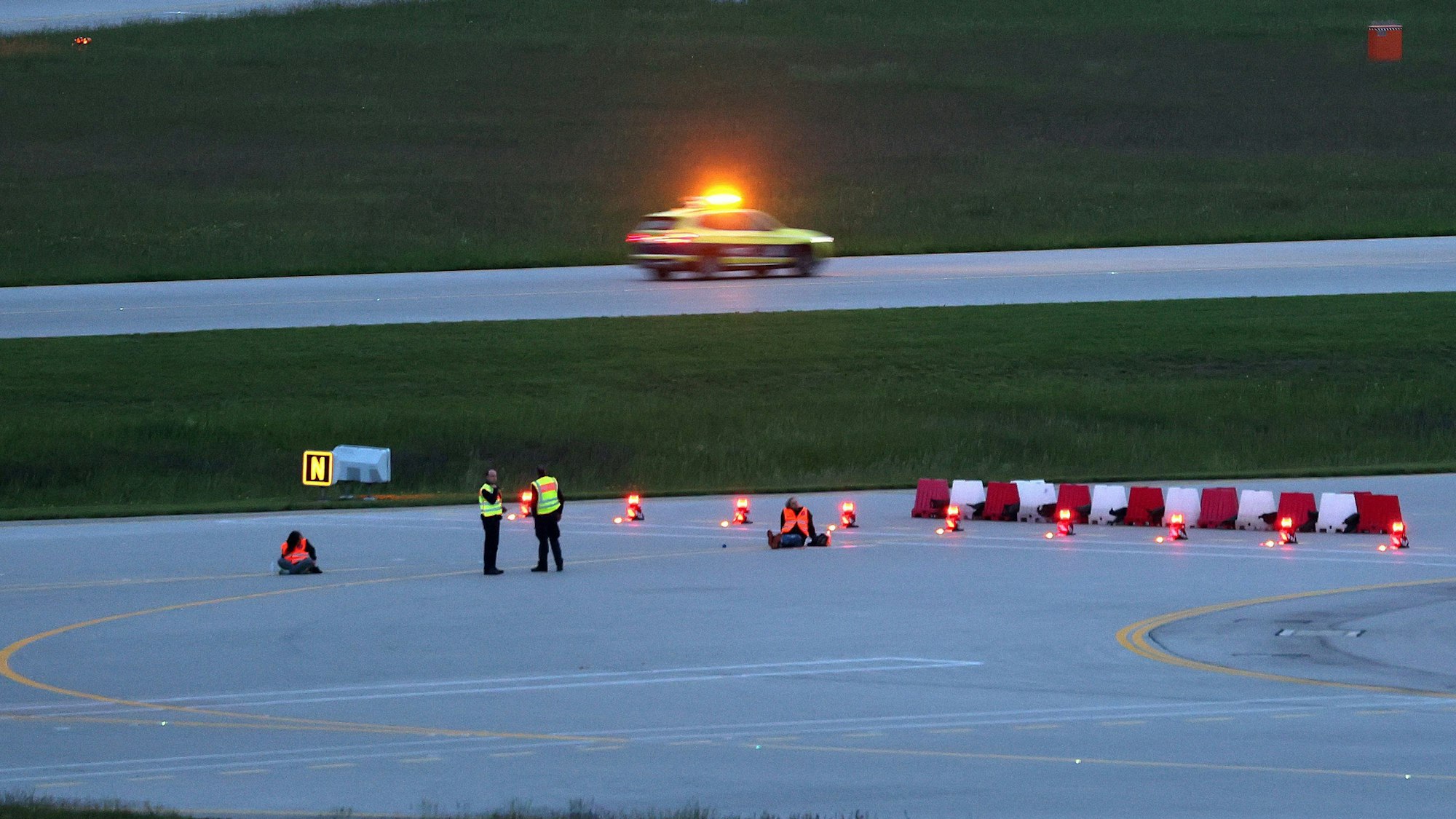 Zwei Klimaaktivisten sitzen auf der Landebahn. Die Polizei ist auch vor Ort.