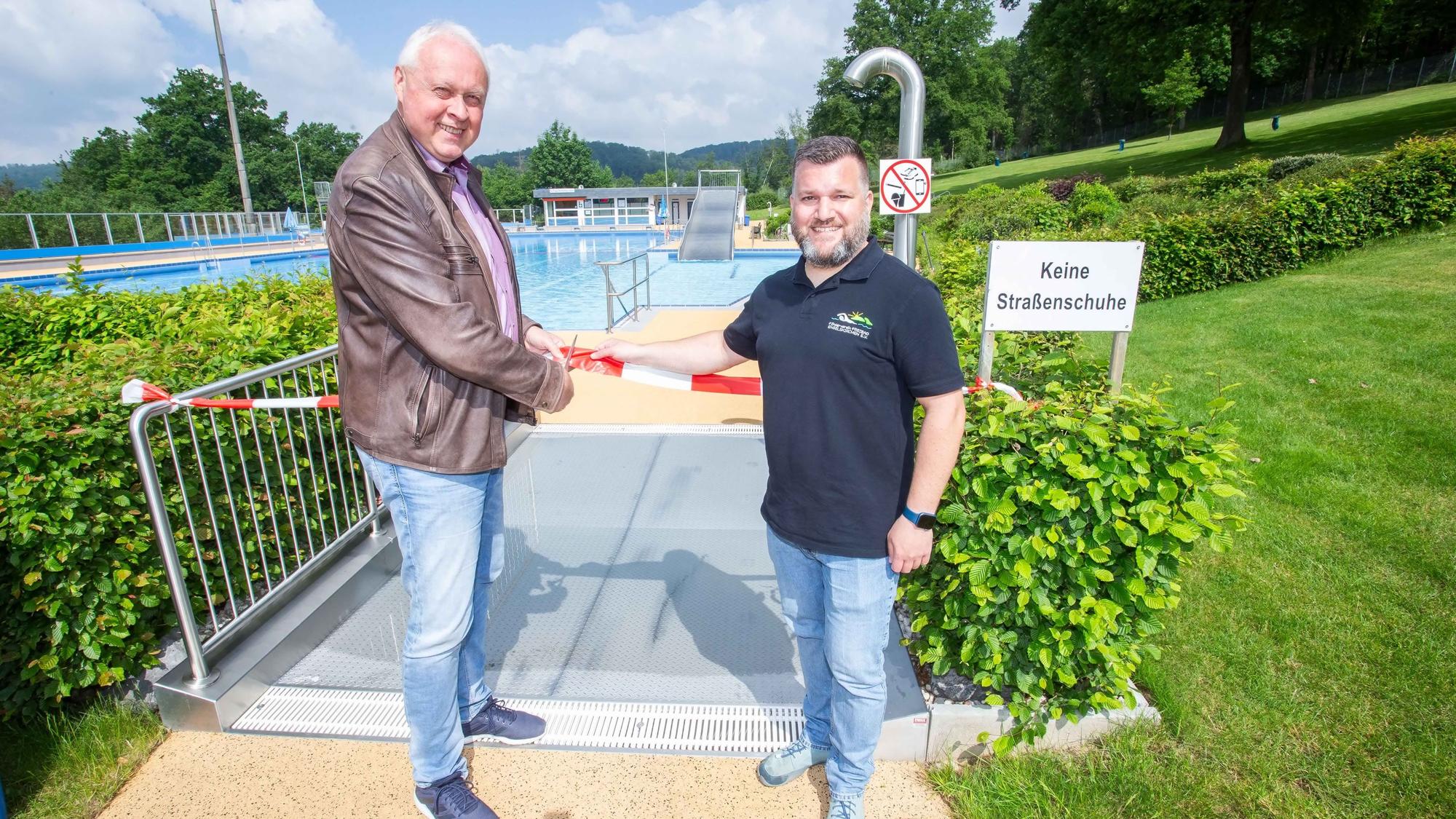Zwei Herren durchschneiden ein Flatterband am Zugang zum Schwimmbecken.