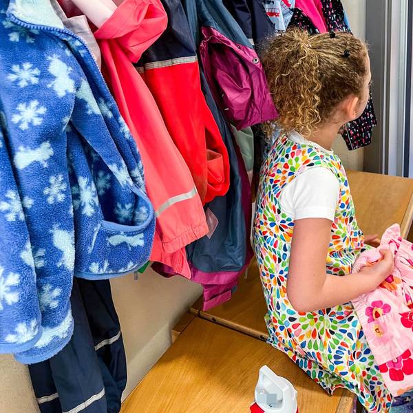 Ein Mädchen sitzt an der Garderobe einer Kindergartengruppe.