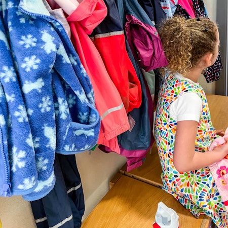 Ein Mädchen sitzt an der Garderobe einer Kindergartengruppe.