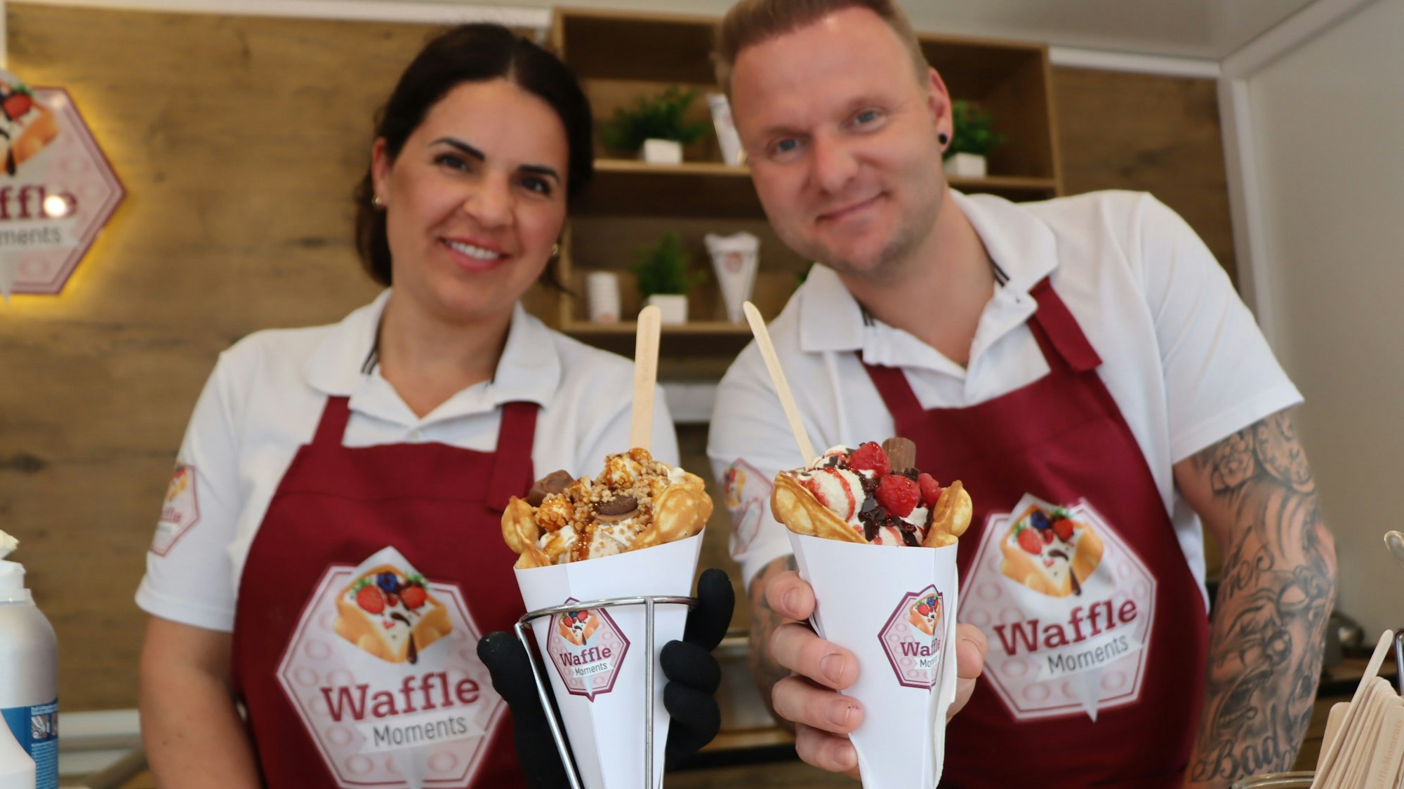 Zwei Personen in Schürzen halten gefüllte Waffeln.