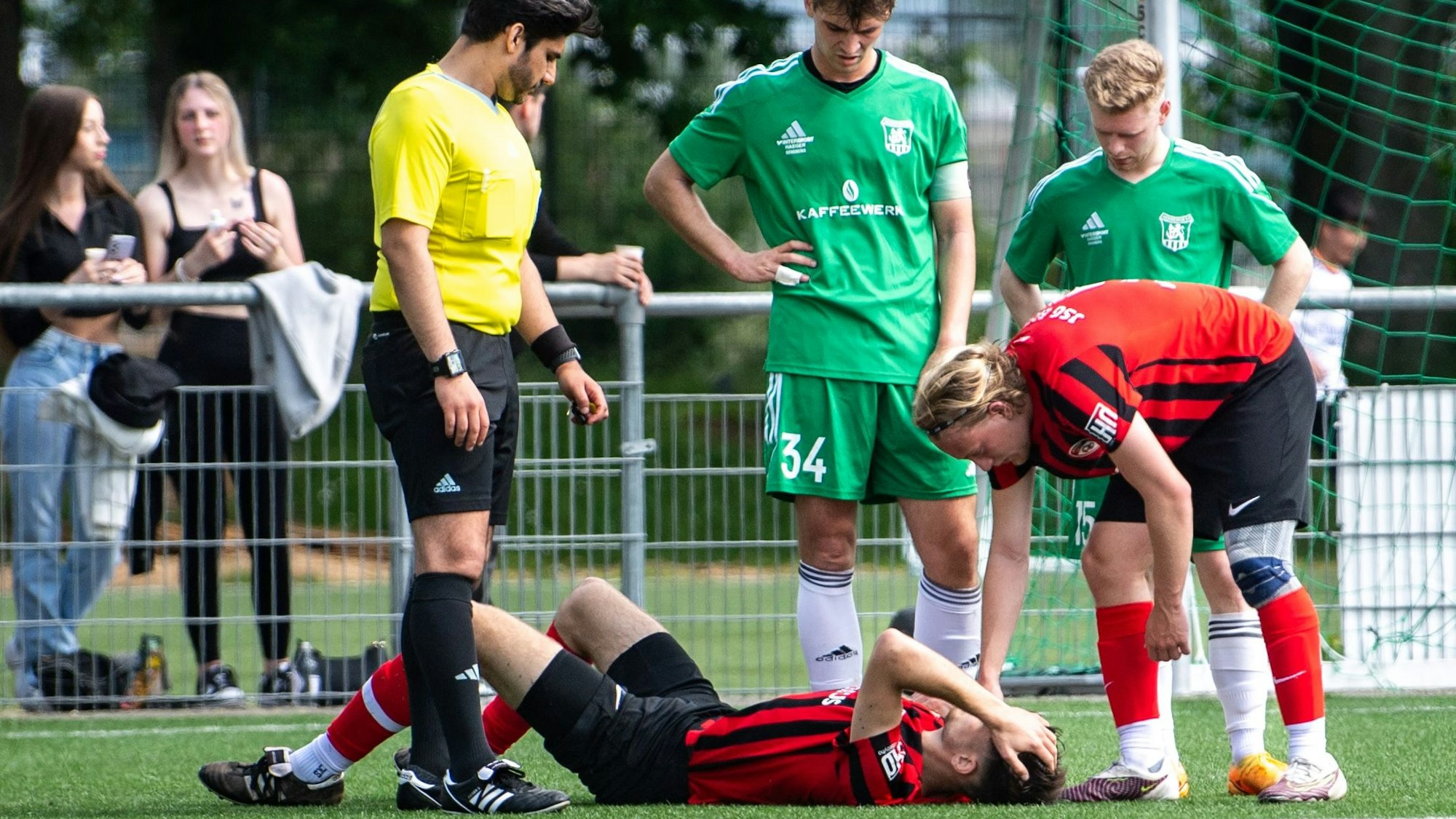 Ein JSG-Erft-Spieler liegt am Boden, die Hände am Kopf. Ein Mitspieler, zwei Gegenspieler und der Schiedsrichter schauen auf ihn.