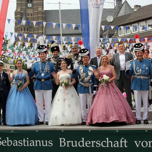 Eine Gruppe von Männern in Schützenuniform und Frauen in Ballkleidern nimmt auf einer Tribüne die Schützenparade ab.