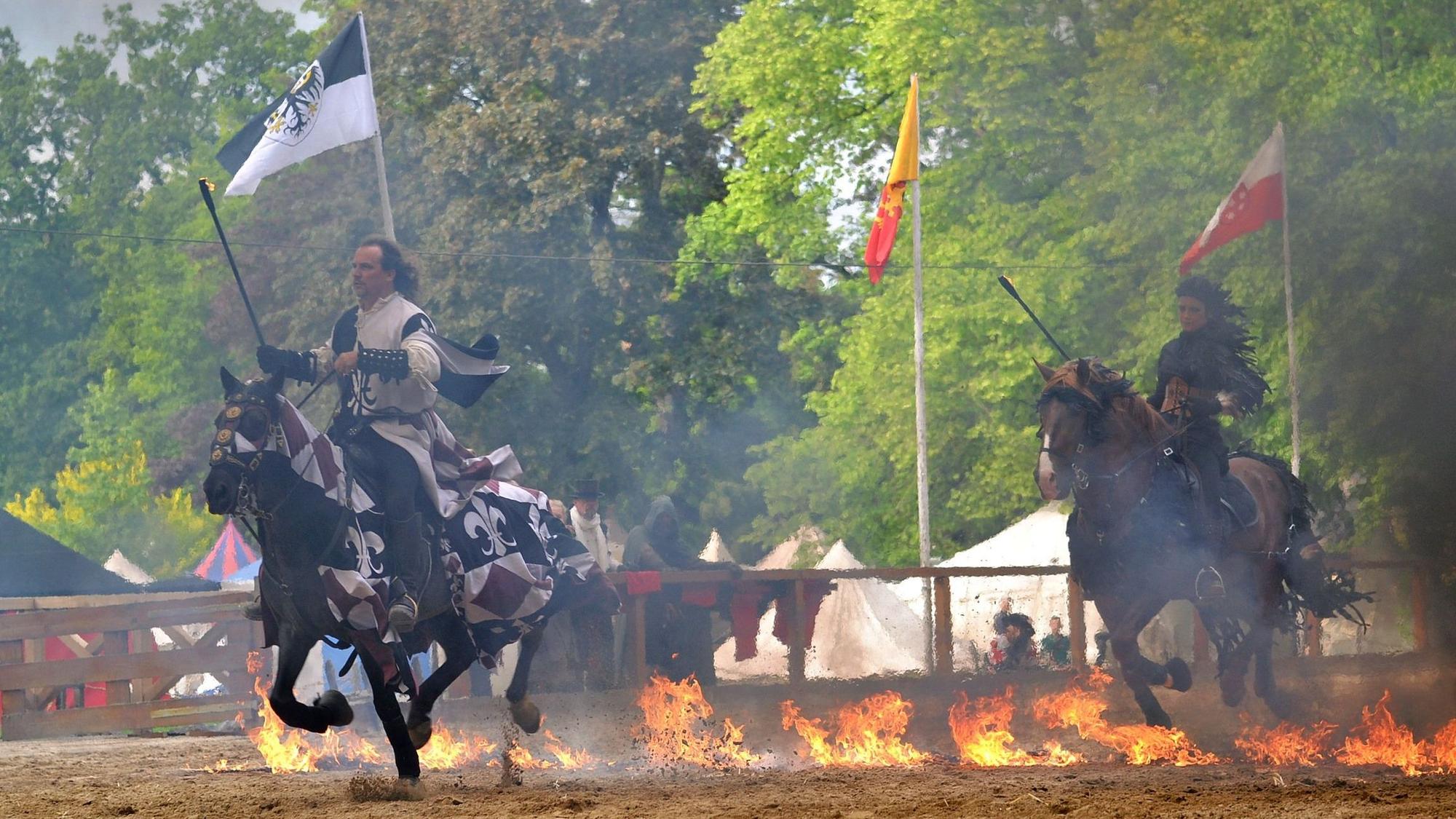 Ein Reiter und eine Reiterin traben mittelalterlich verkleidet mit ihren Pferden durch eine Feuerlinie.