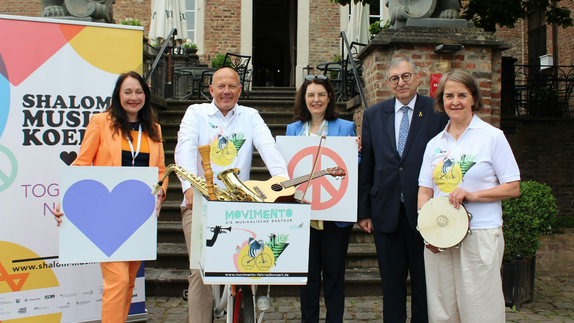 Drei Frauen und zwei Männer stehen mit Plakaten und Musikinstrumenten vor der Treppe von Schloss Loersfeld.