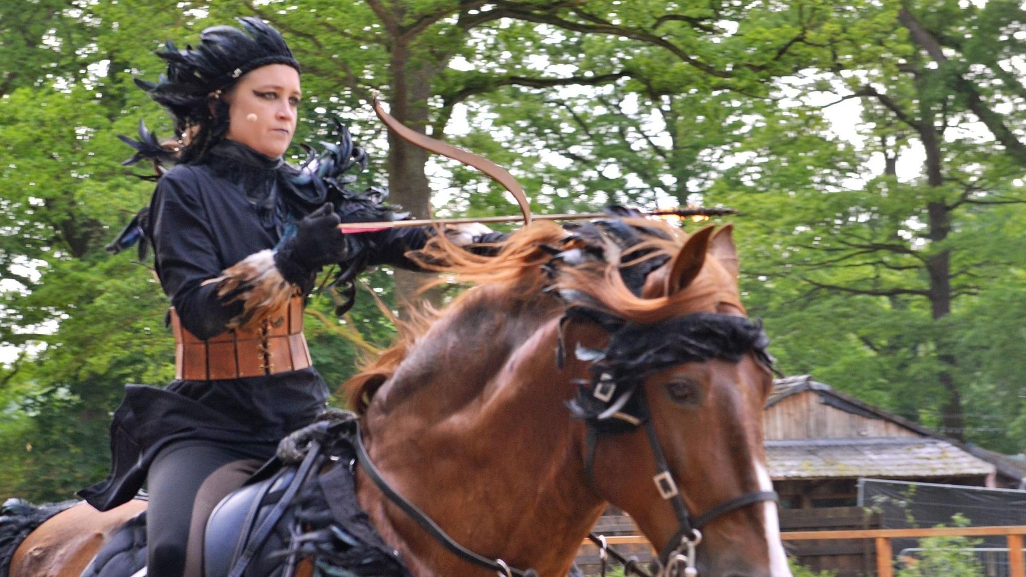 Gastgeberin Patricia Gräfin Beissel reitet mit Pfeil und Bogen auf einem Pferd.
