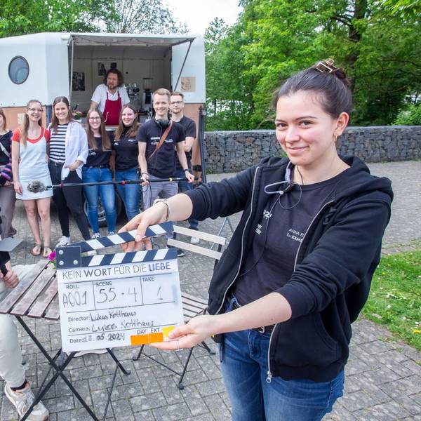 Eine junge Frau hält im Vordergrund eine Klappe hoch, dahinter hat sich das Filmteam versammelt.
