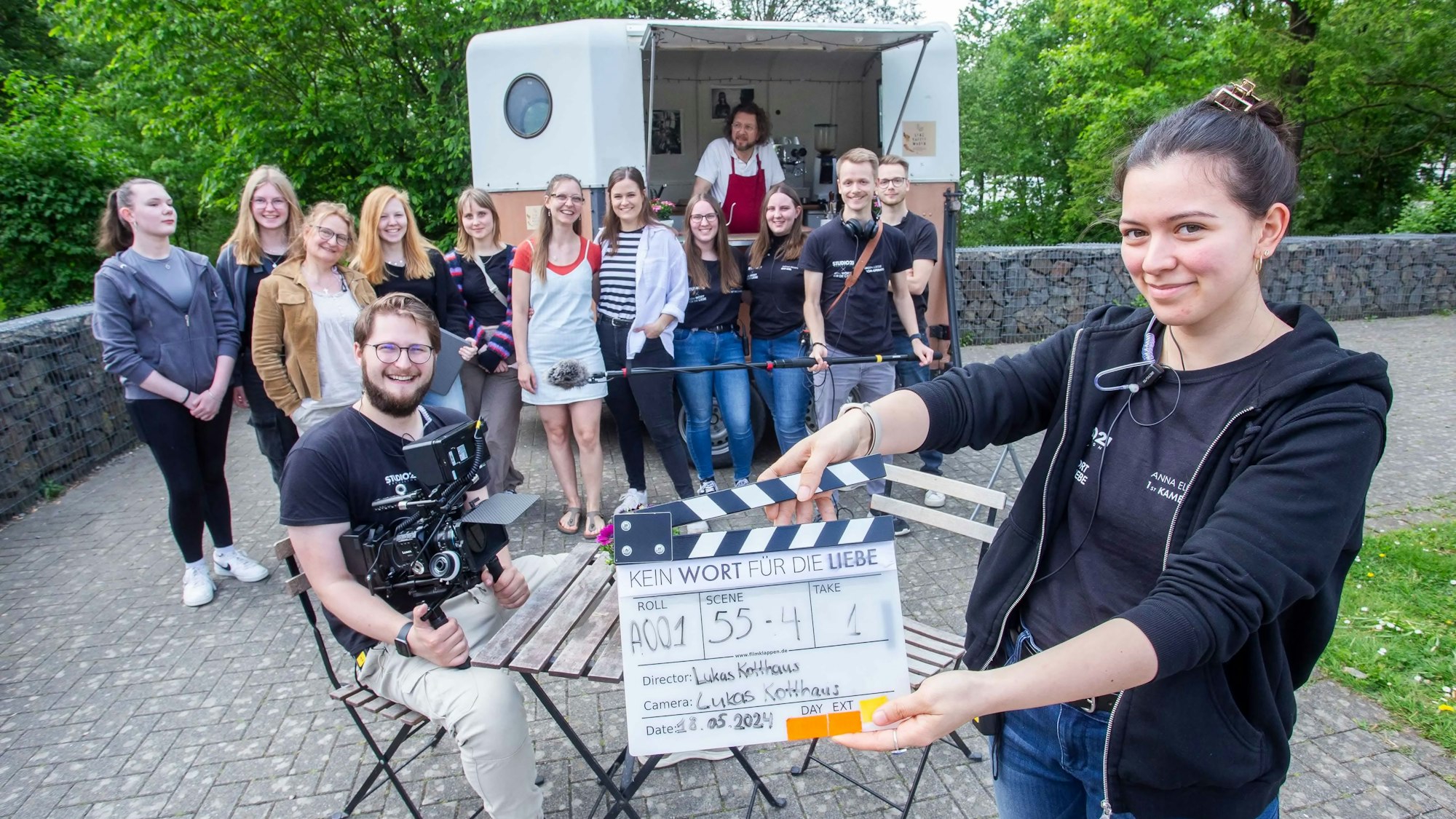 Eine junge Frau hält im Vordergrund eine Klappe hoch, dahinter hat sich das Filmteam versammelt.